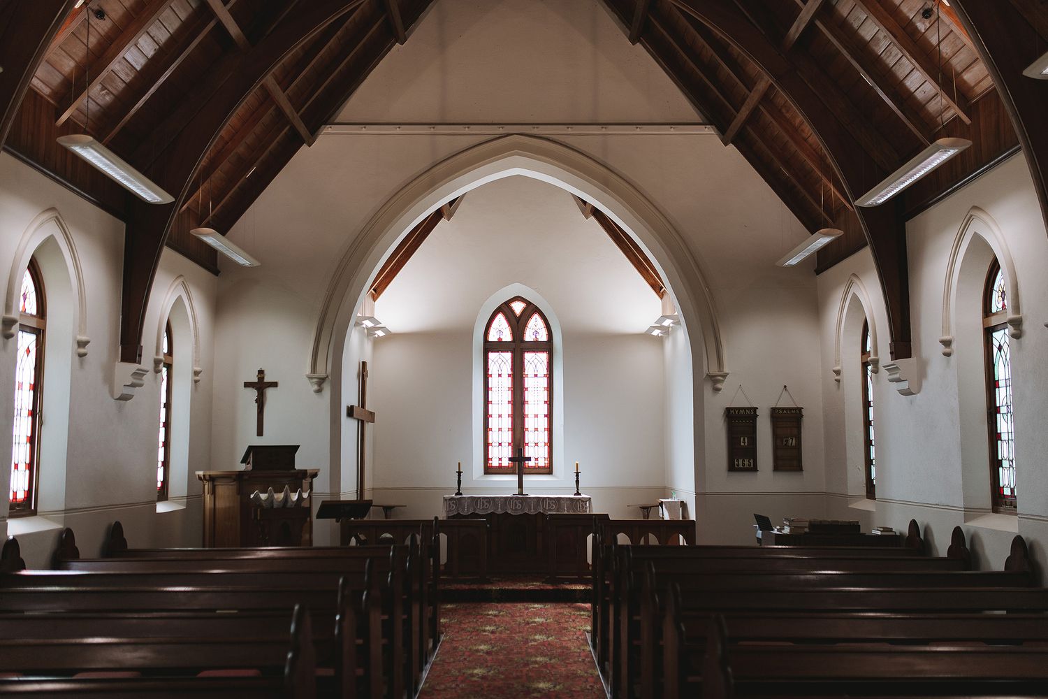 Panoramic view of an empty traditional church interior with white walls, wooden beams, and stained glass windows.