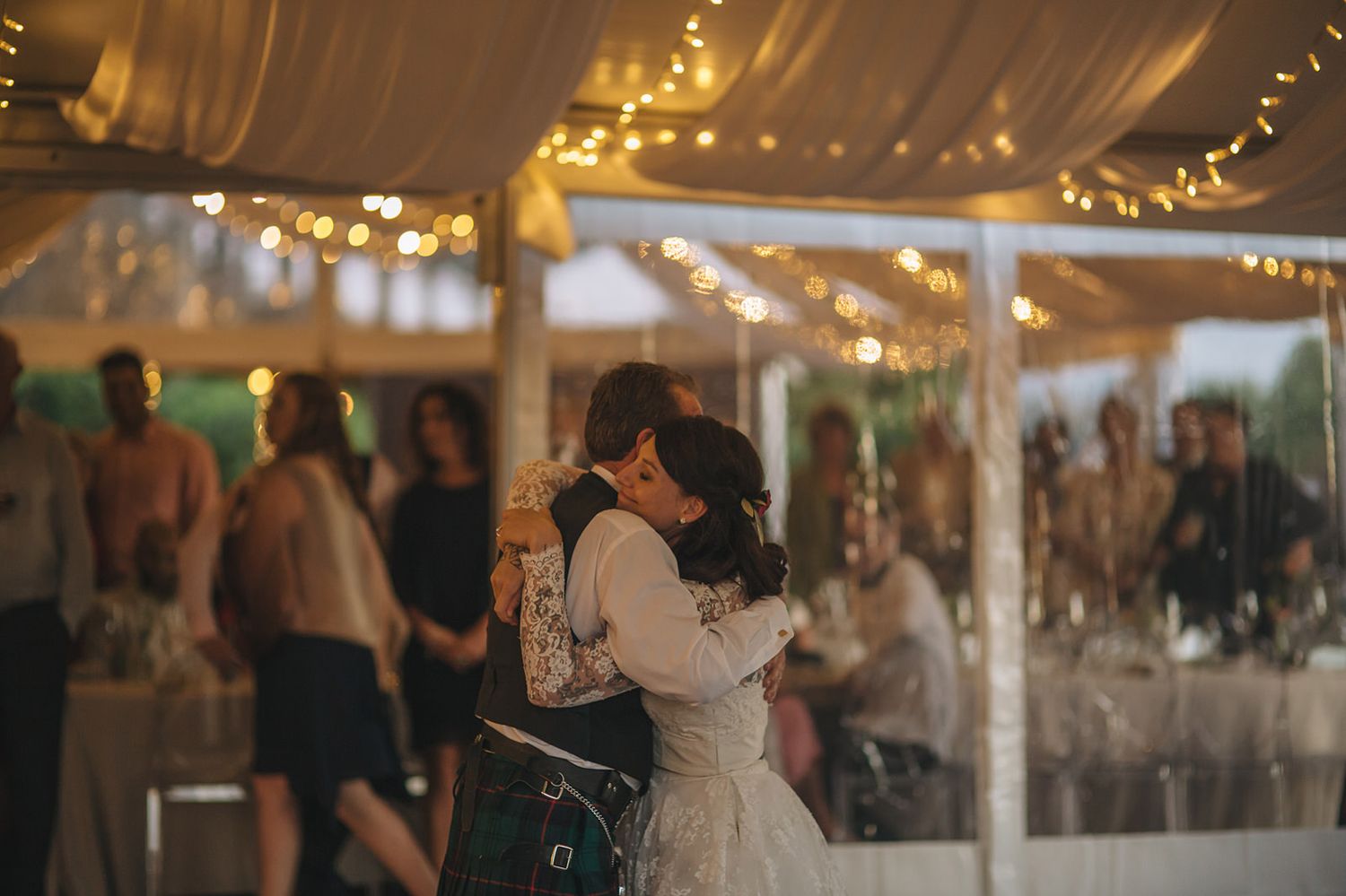 A couple shares an intimate dance under a twinkling tent canopy at an evening wedding reception.