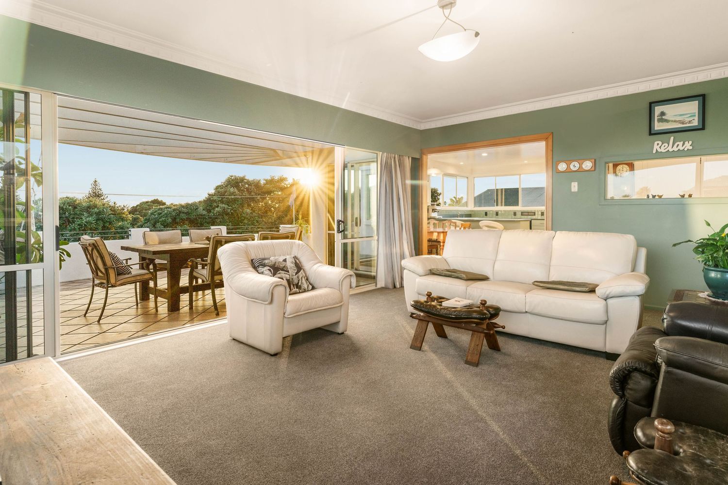Modern living room with white sofas opening to outdoor balcony with dining area and sunset views.