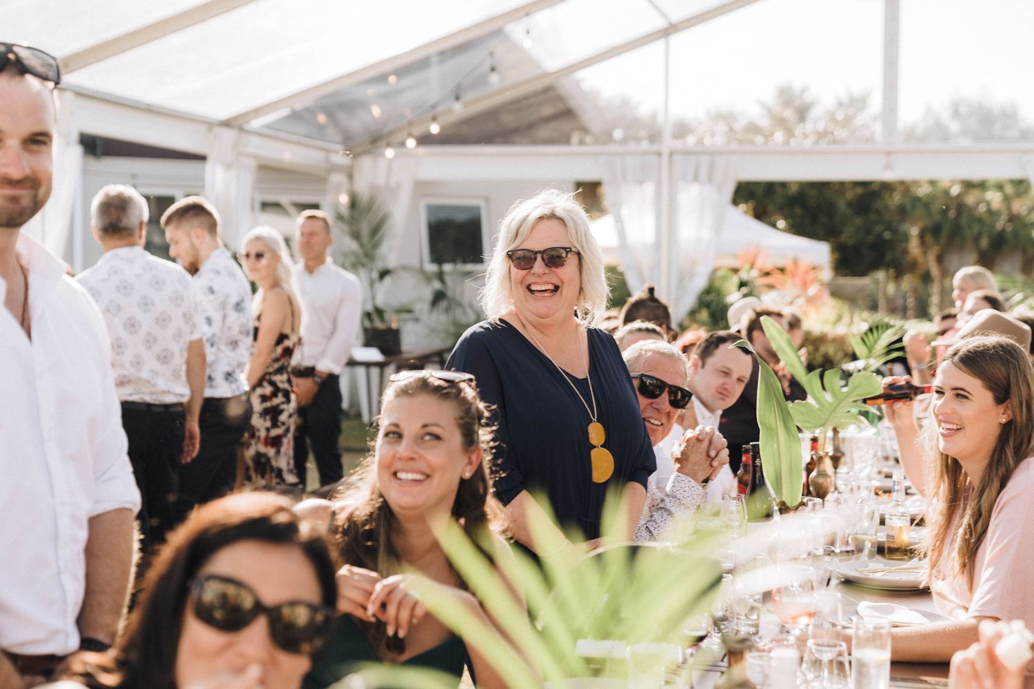 Wedding guests mingling and celebrating at an outdoor reception under a white tent.
