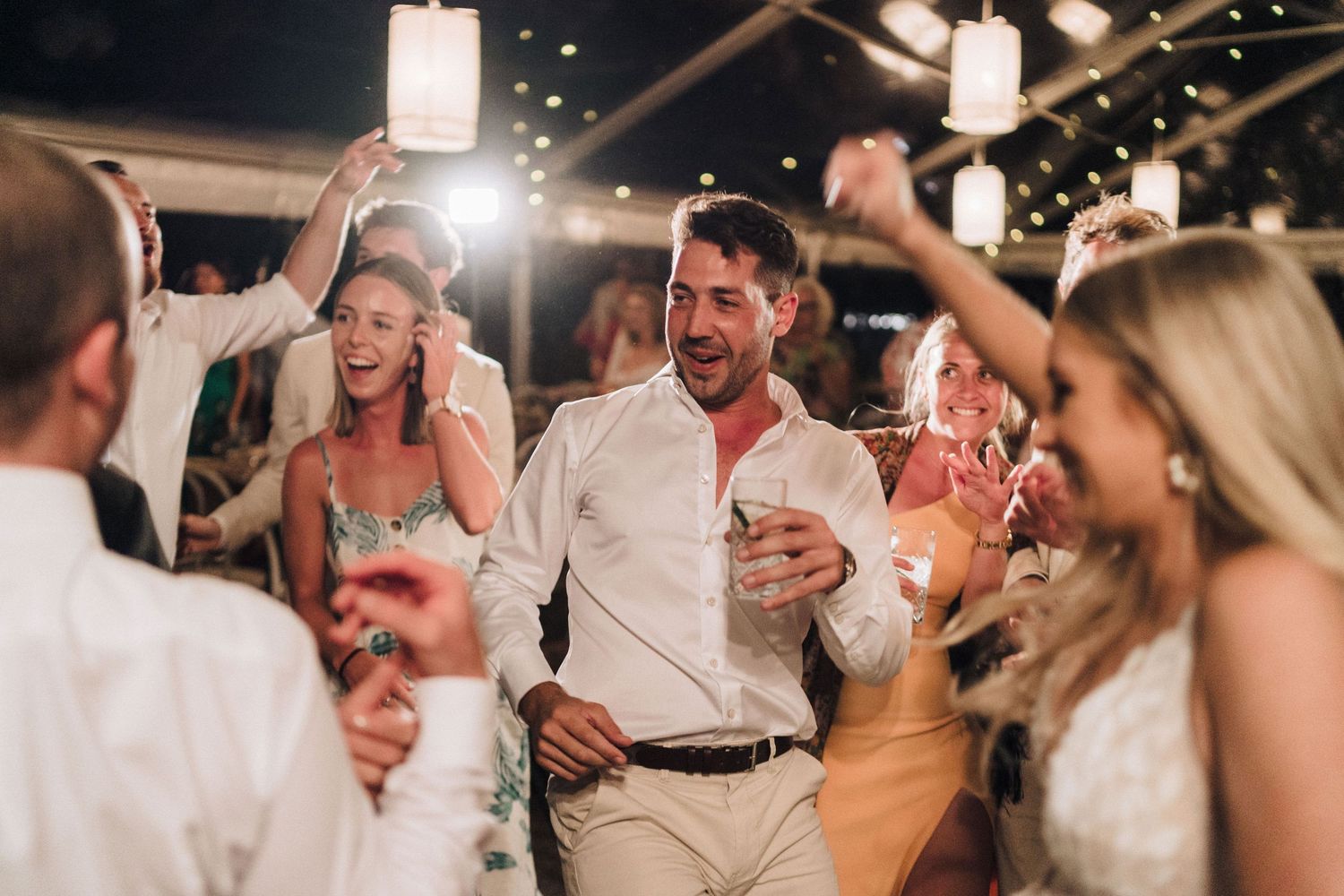 Wedding reception dance party with festive lighting and guests celebrating on the dance floor.