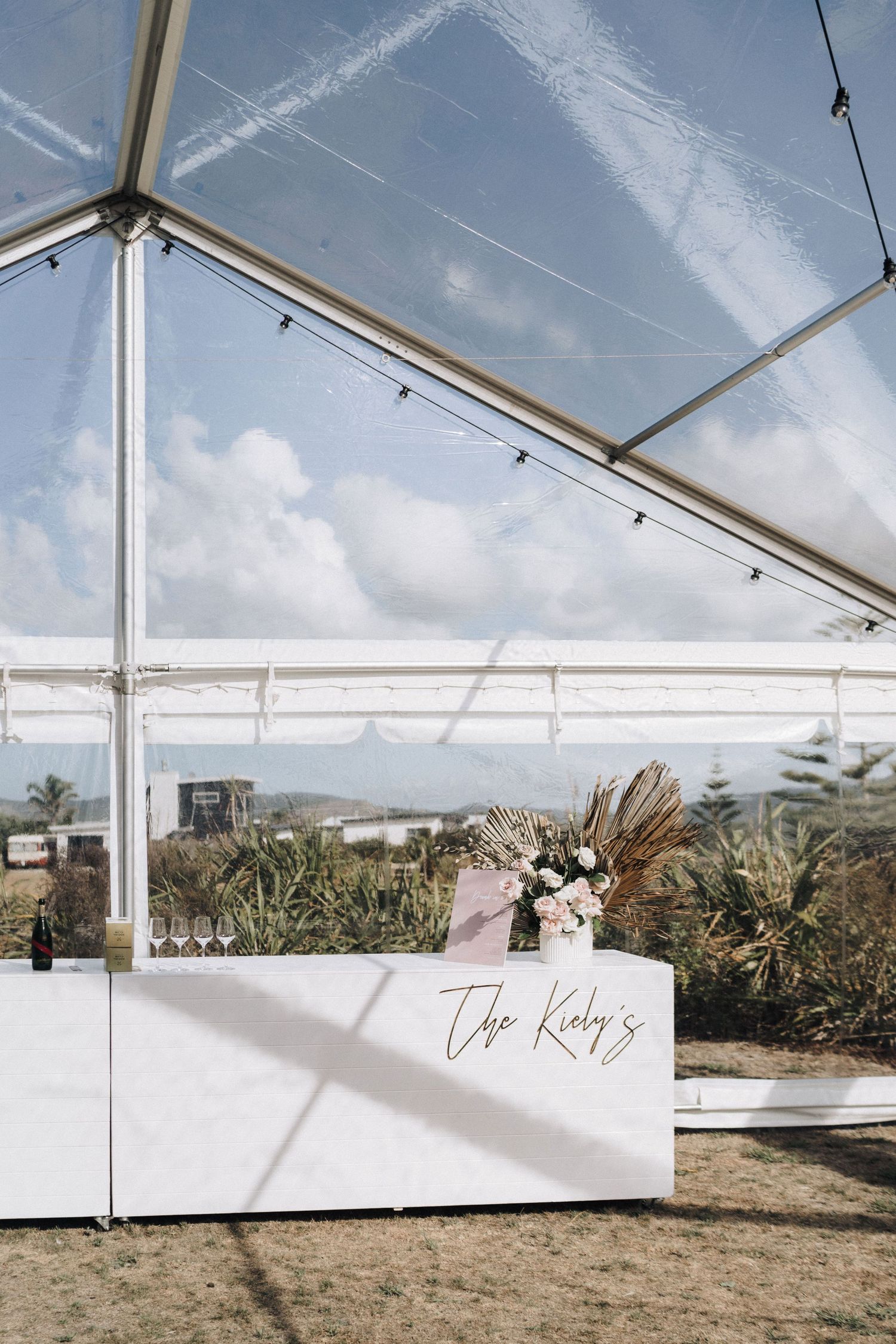 Clear marquee tent set up for a beach wedding with scenic coastal views in the background.