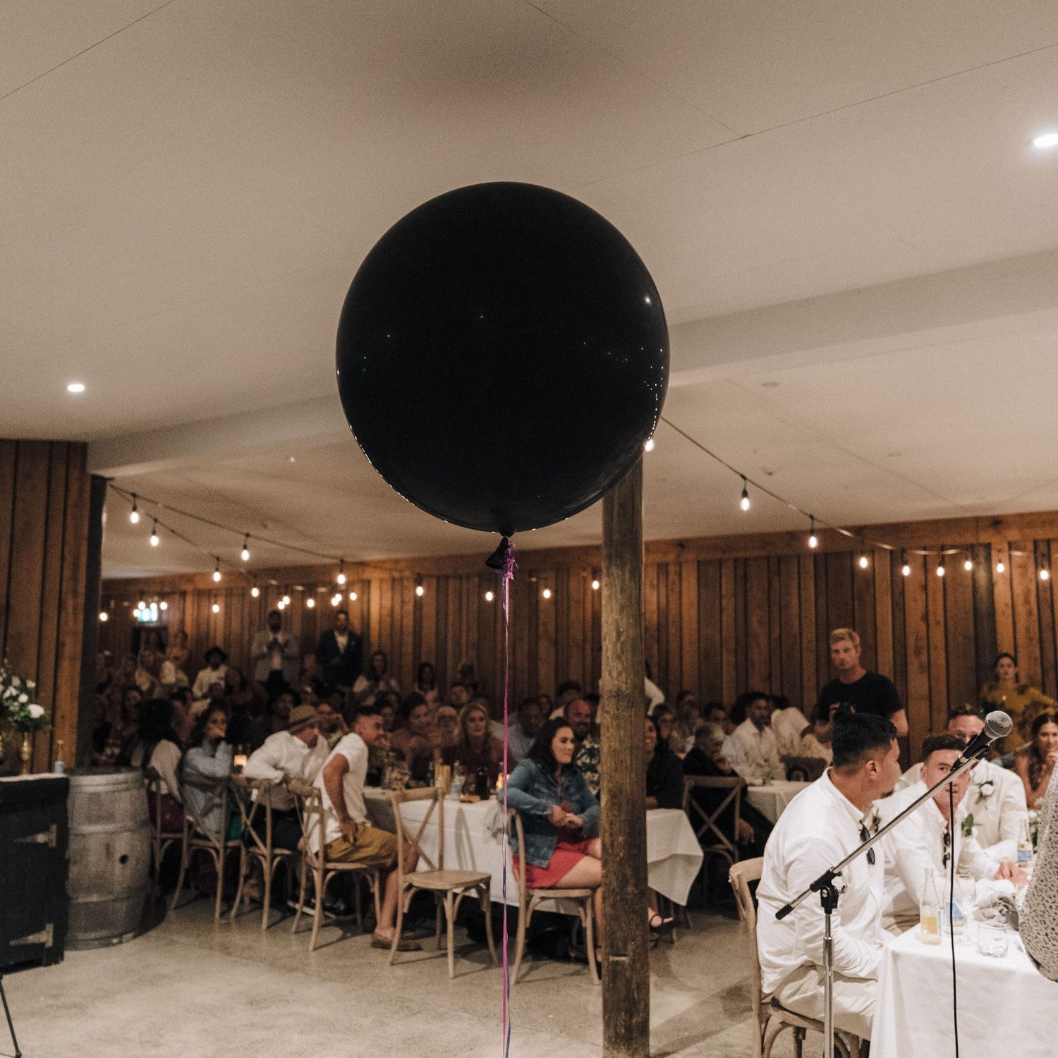 Reception venue with wooden walls decorated with string lights and a large black balloon centerpiece.