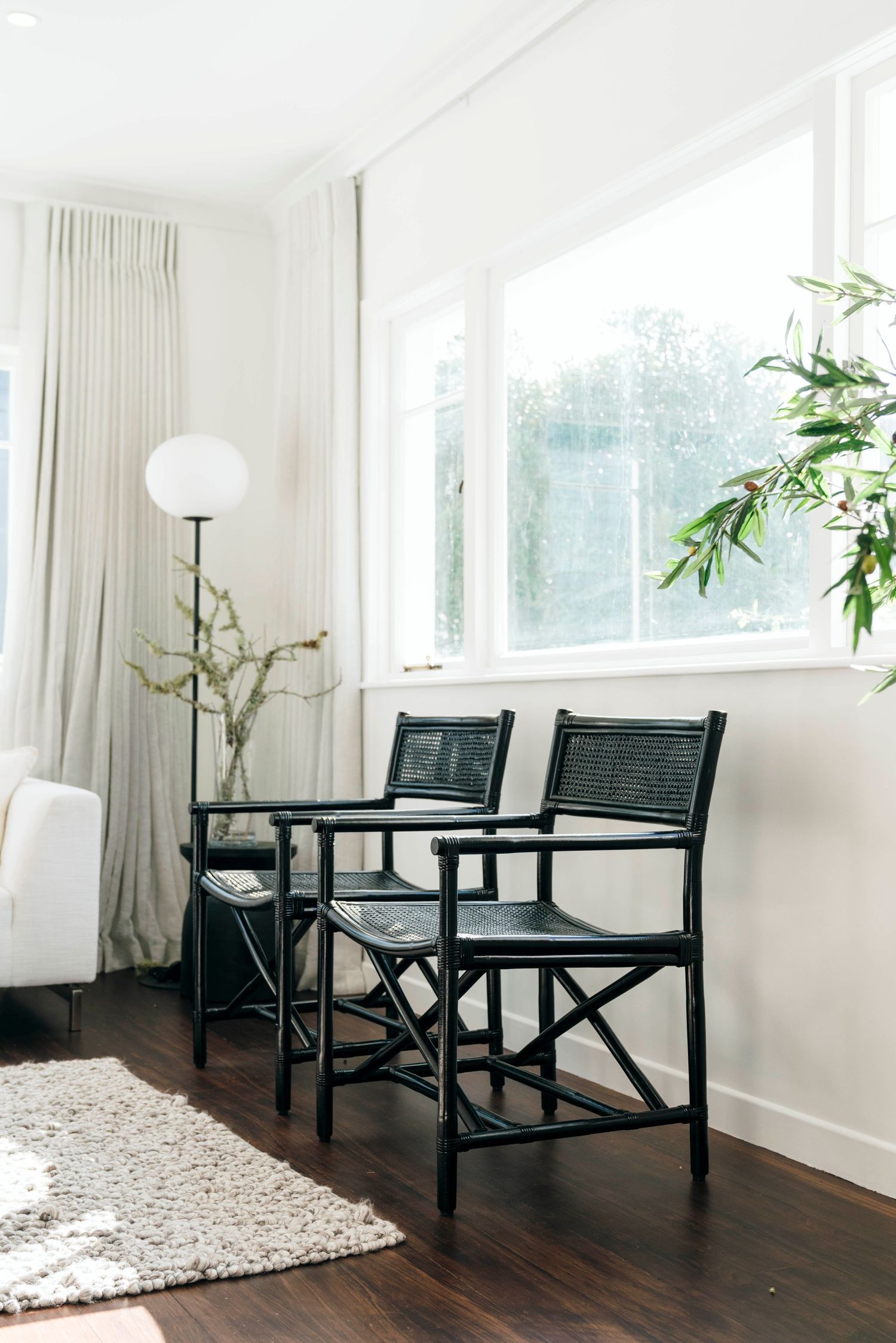 Modern black chairs and side tables arranged in a bright white room with large windows and potted plants.
