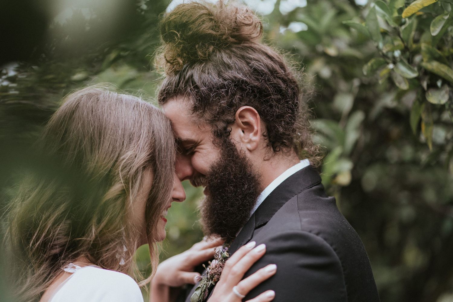 A romantic moment between a couple touching foreheads amidst green foliage in an intimate outdoor setting.