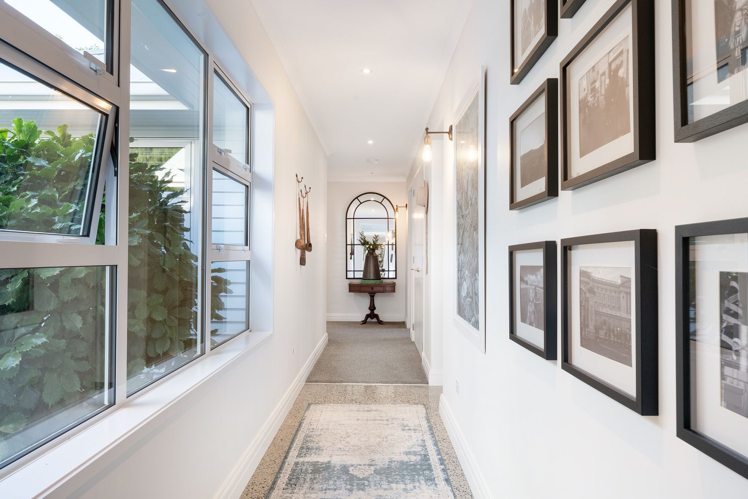 Bright hallway with gallery wall, decorative mirror, and large windows letting in natural light.