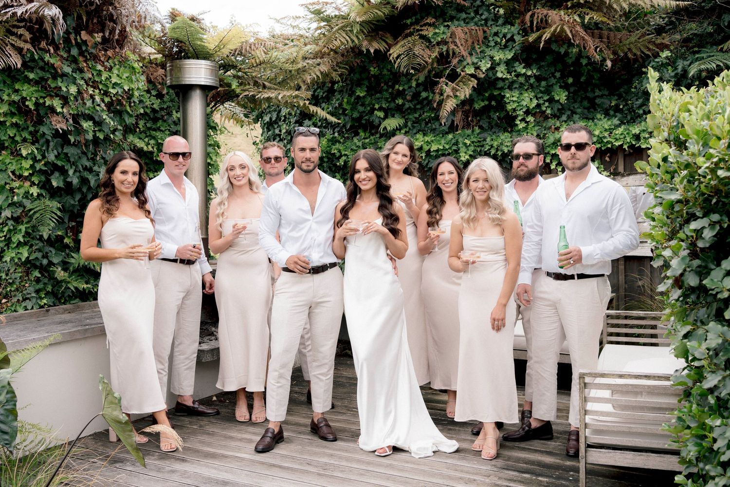 Wedding party dressed in all white poses together in a garden setting for an elegant outdoor photo.