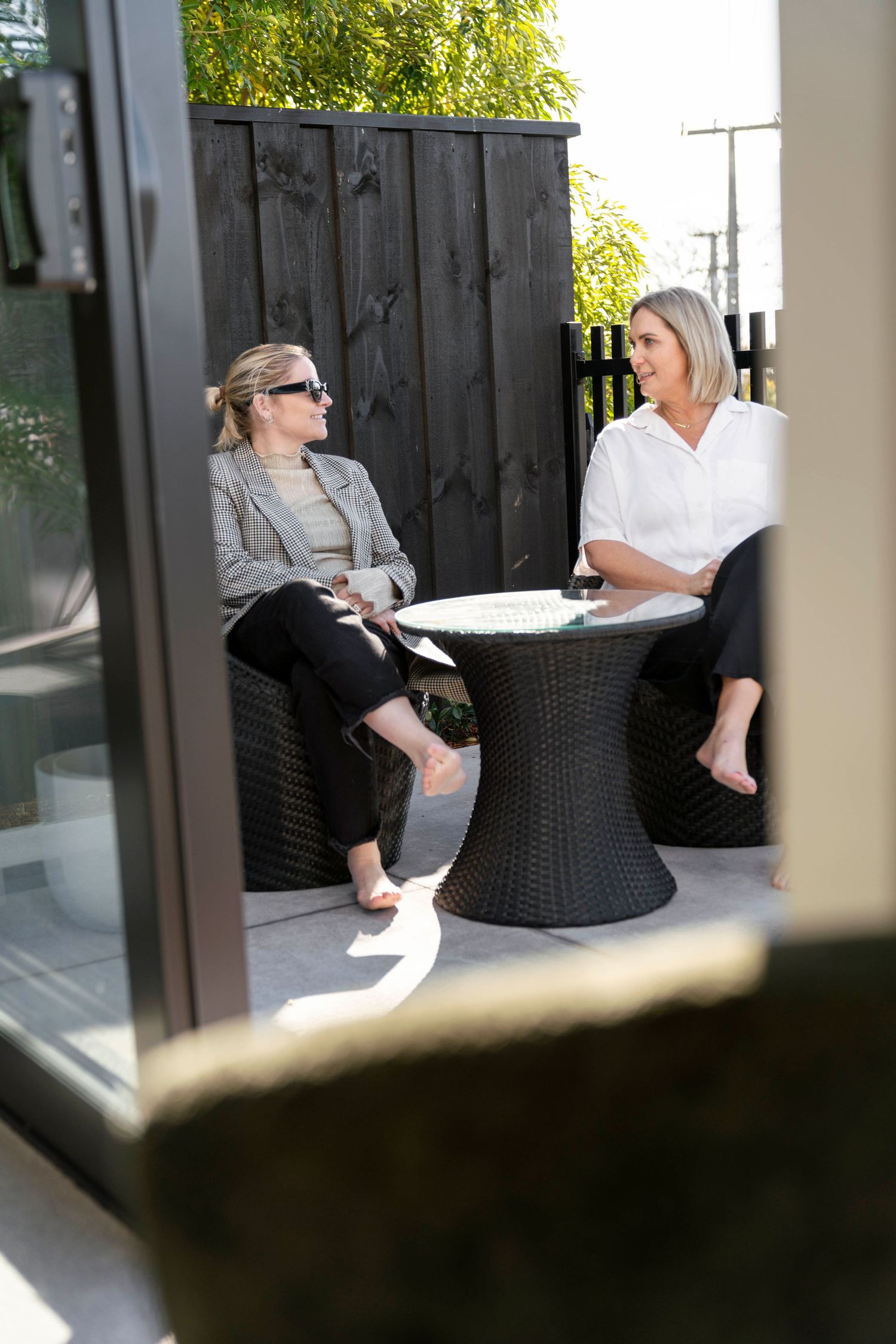 Two wicker chairs sit on an outdoor patio with lush greenery visible in the background.