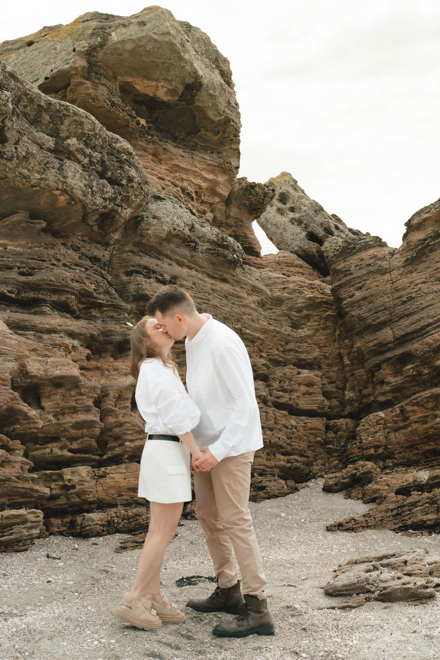 A romantic couple shares an intimate moment on a rocky beach surrounded by cliffs.