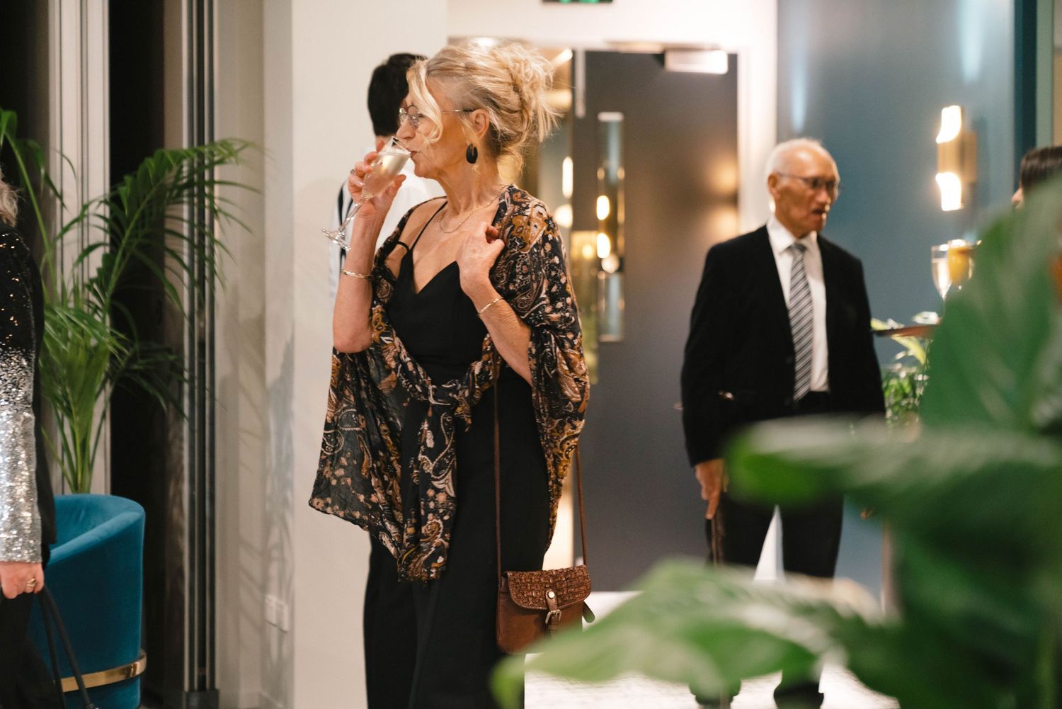 Elegantly dressed people standing in a modern office hallway with plants and ambient lighting.