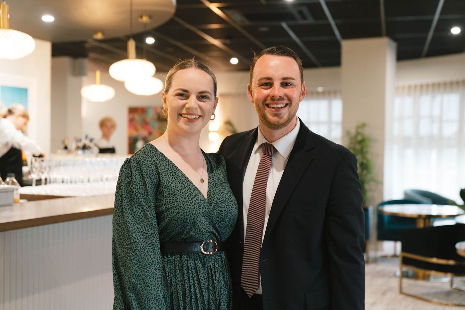 Guests in formal attire pose together at an indoor reception venue with modern furnishings.