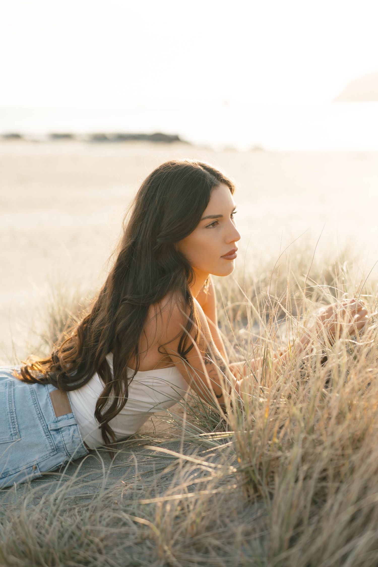 Woman lounging in tall grass during golden hour with wind-swept hair.