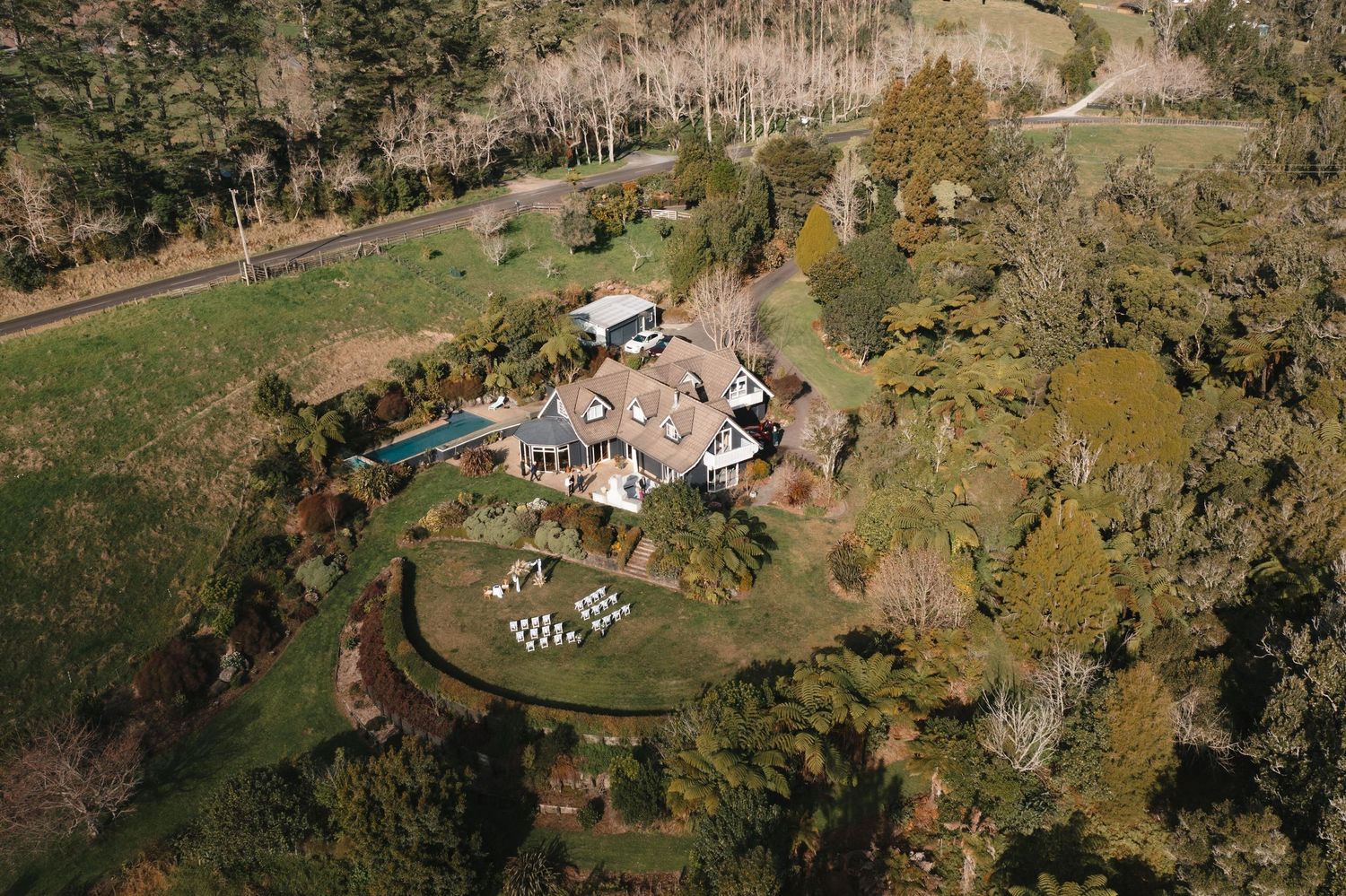 Aerial drone view of a rustic property with multiple buildings nestled in rolling countryside with autumn trees.