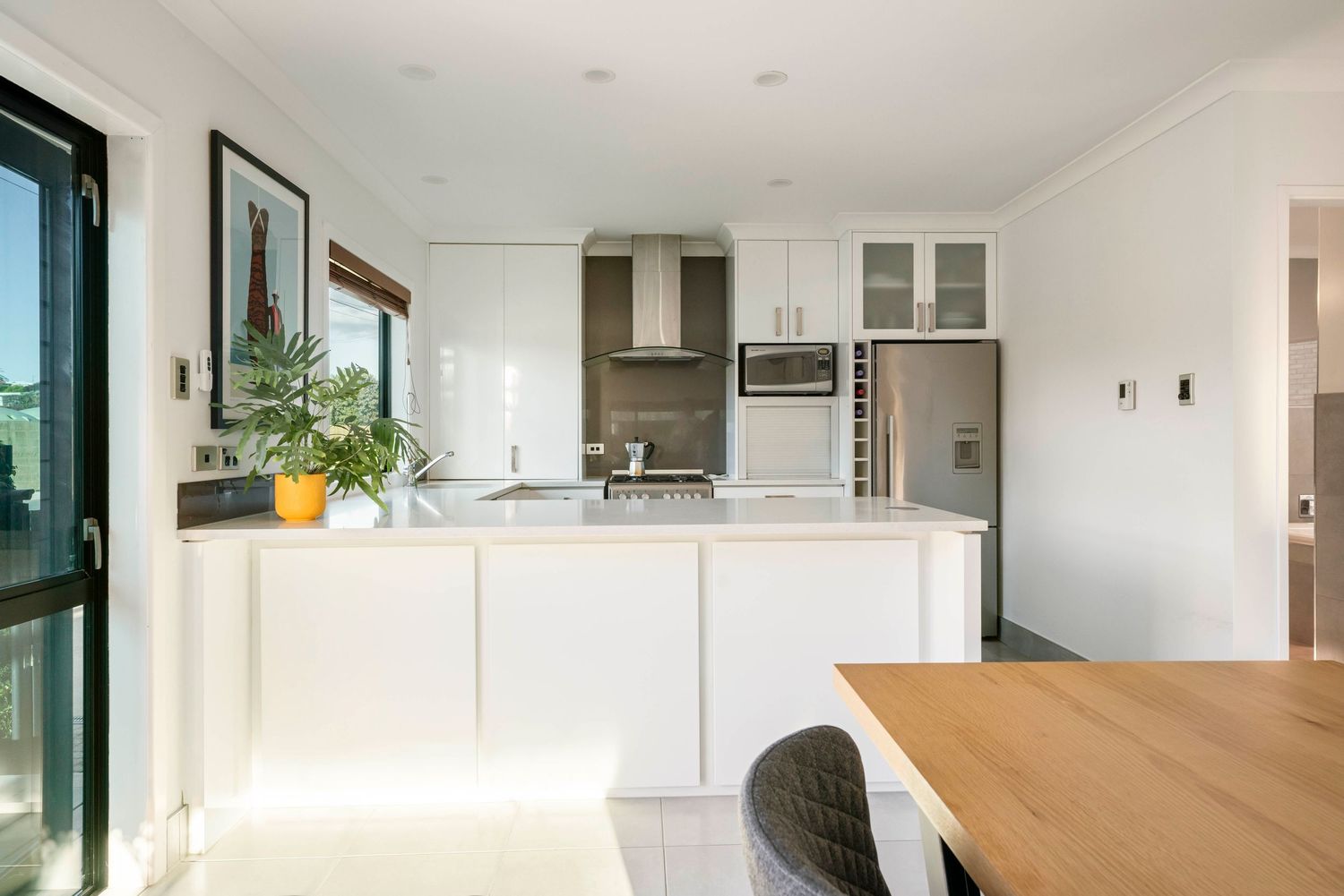 Contemporary white kitchen with wooden dining table and stainless steel appliances in open concept space.