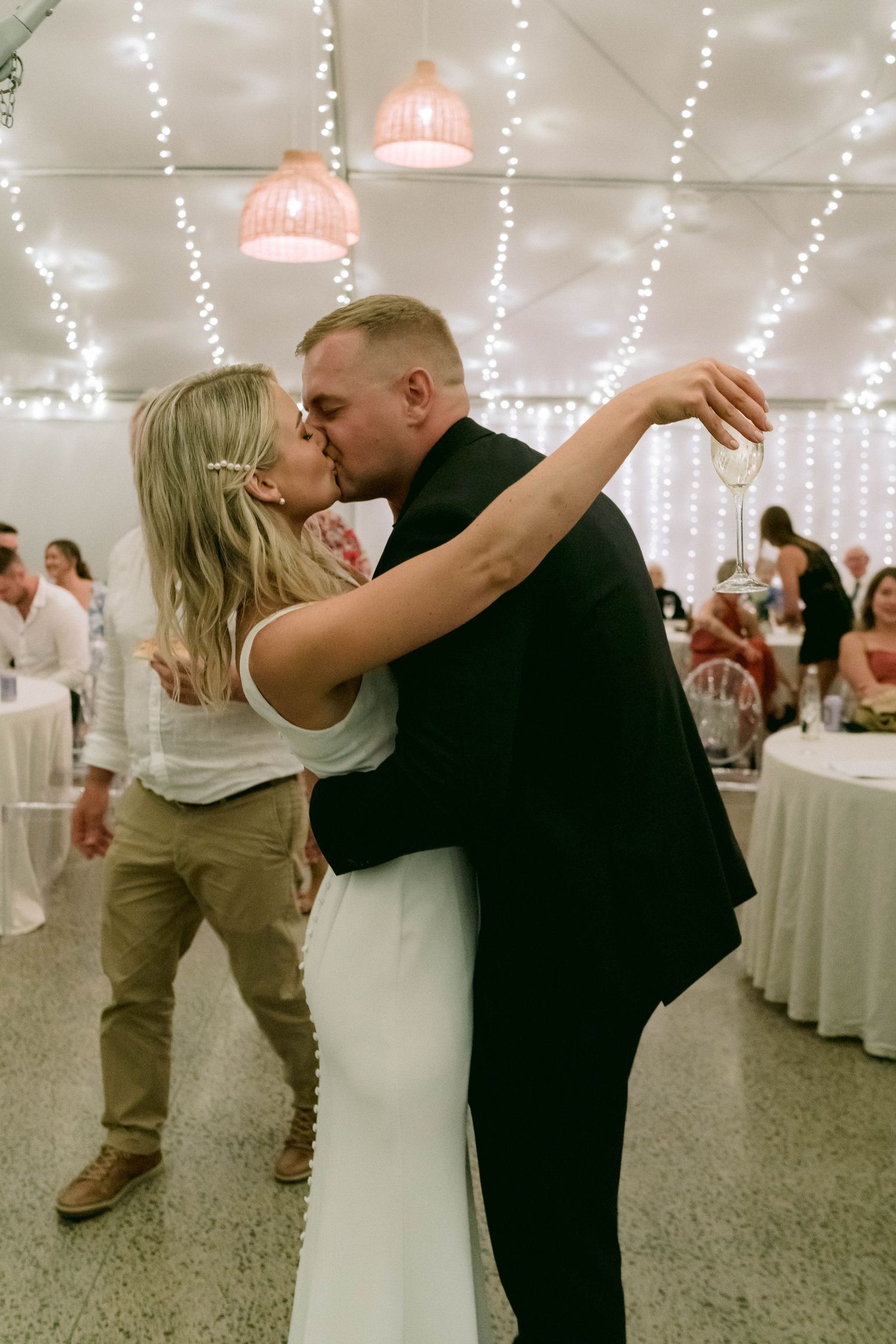 A couple shares their first dance in a tent decorated with string lights.