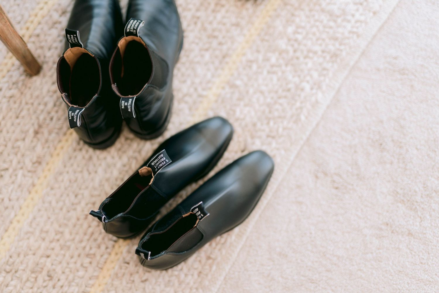 Two pairs of black leather ankle boots arranged on a beige carpet floor.