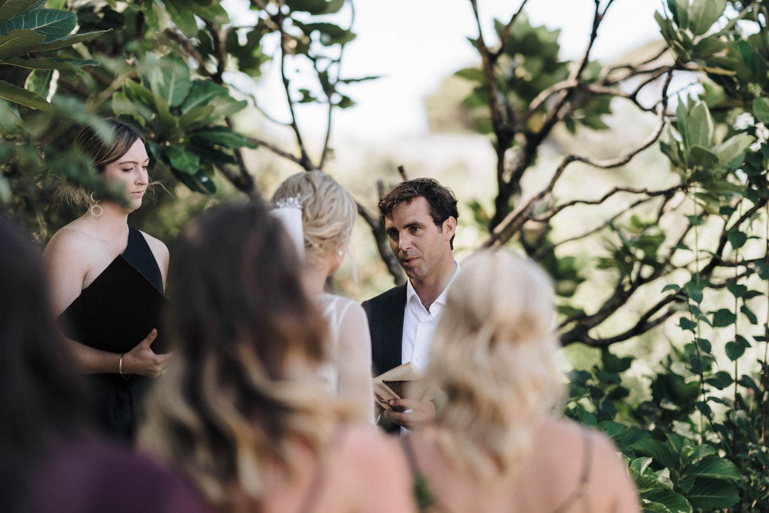 A small wedding ceremony takes place outdoors among green leaves and foliage.