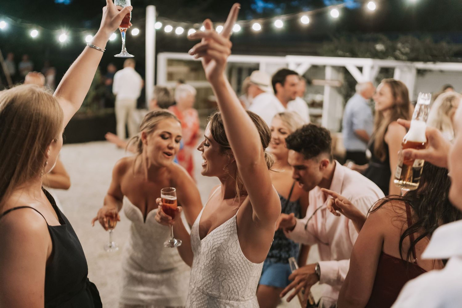 Wedding party guests raise their hands and dance together on the dance floor during an indoor reception celebration.