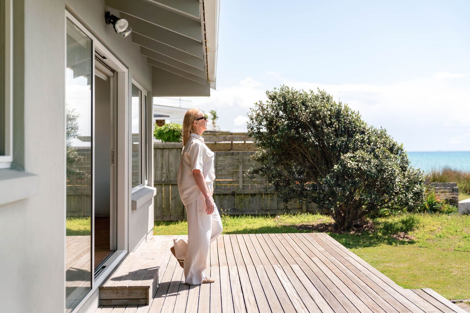 A coastal beach house with a wraparound wooden deck and bright white exterior offers scenic ocean views.