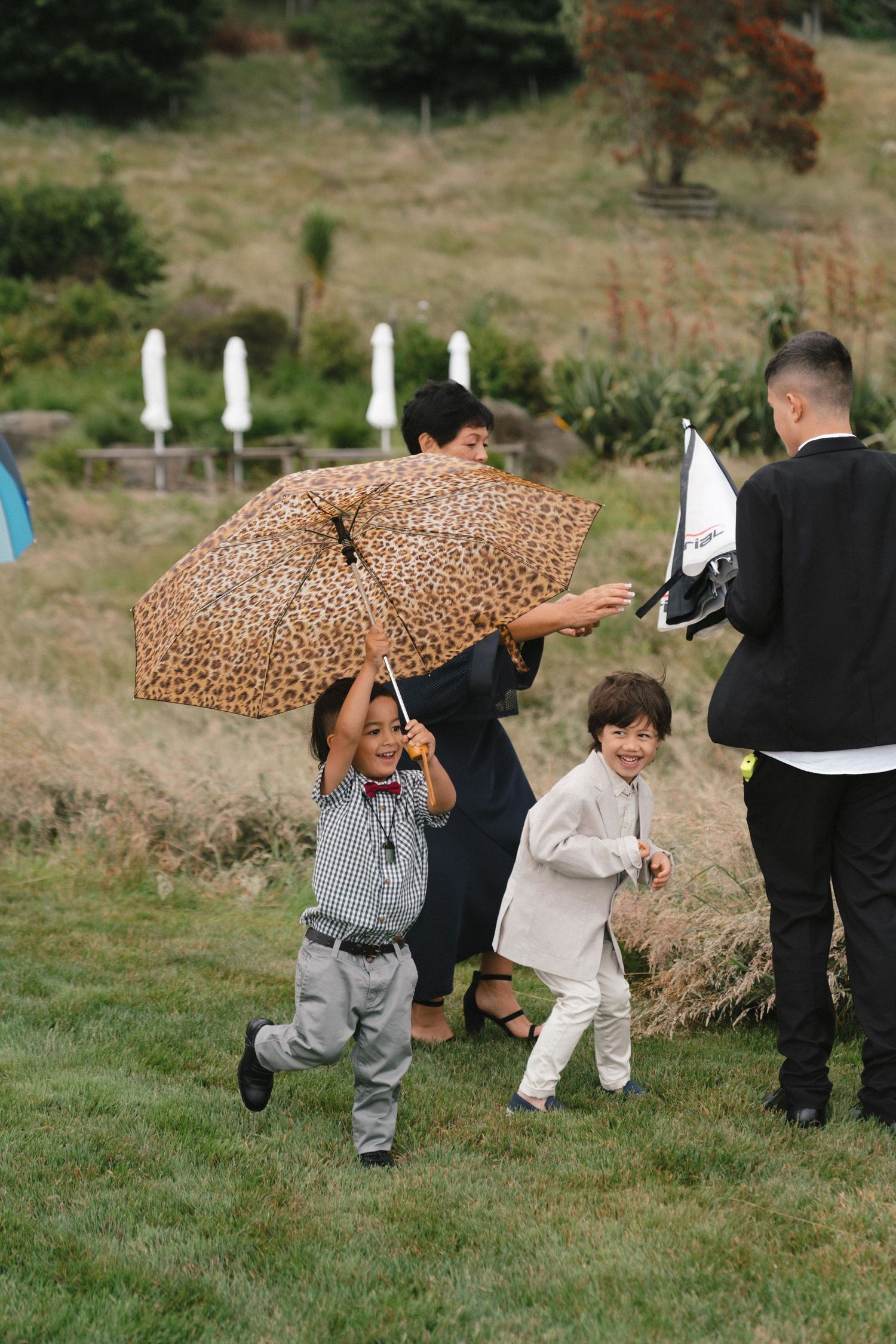 Humorous sequence of children ducking under a leopard print rain umbrella during an outdoor event.