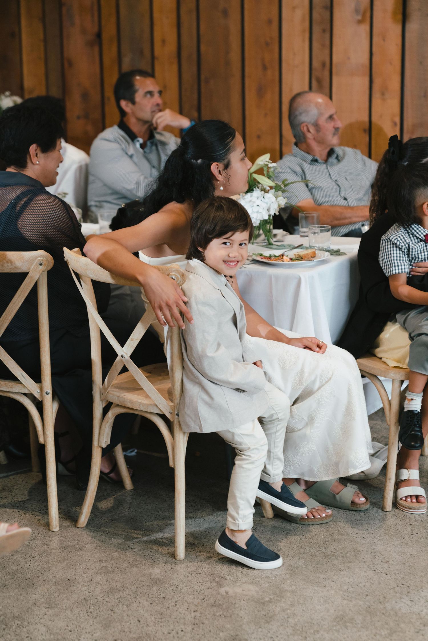 Wedding reception guests relax in rustic wooden chairs during casual dinner gathering.