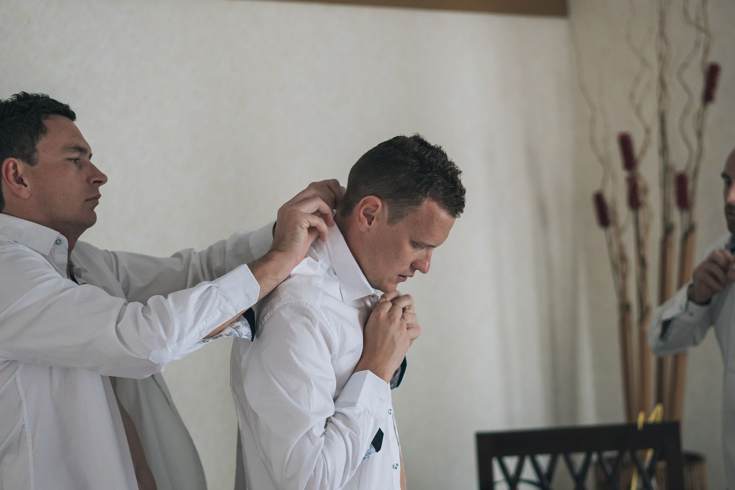 A person in a white button down shirt is helped with formal attire while getting dressed.