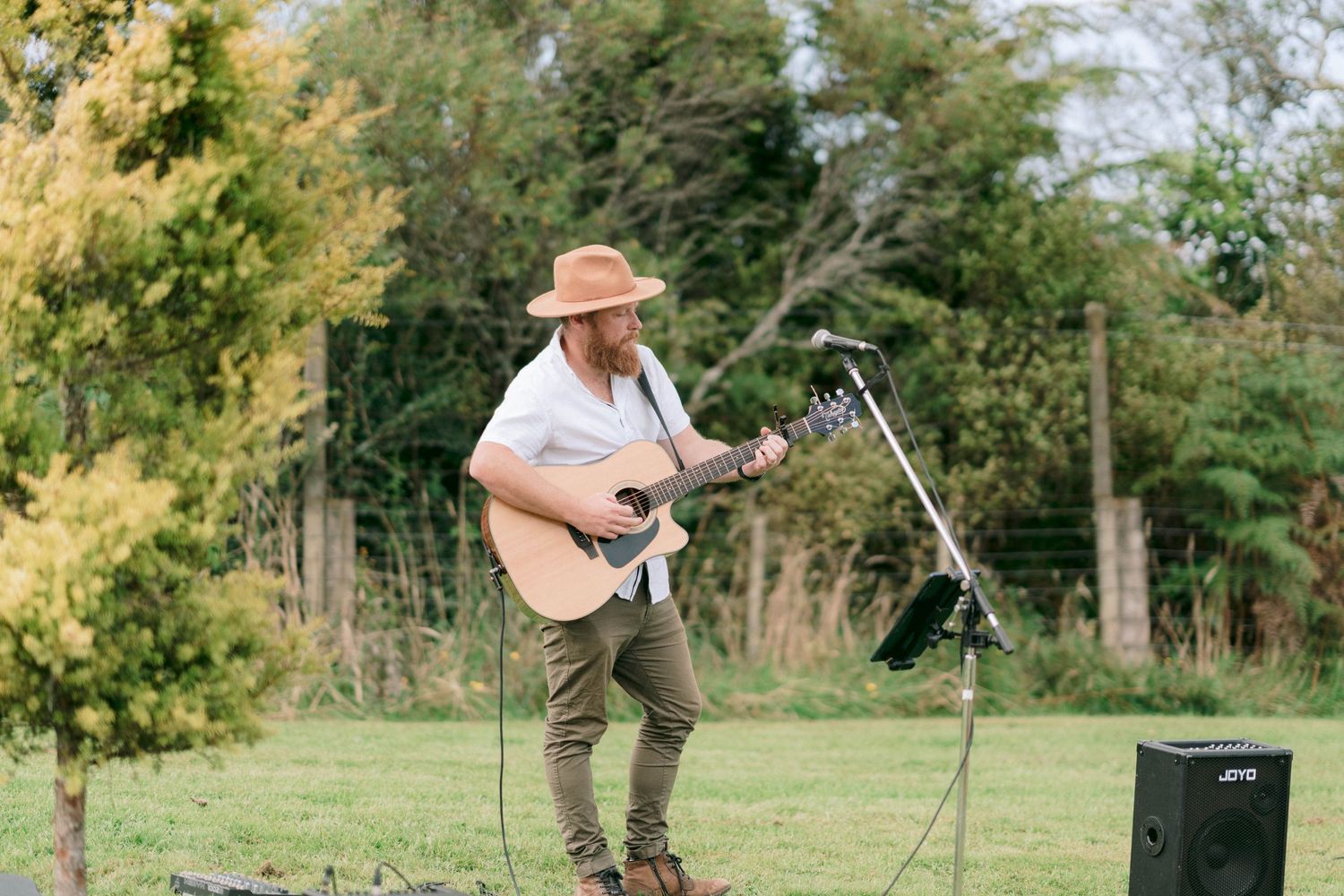 Musician in casual attire performs with acoustic guitar at outdoor event.