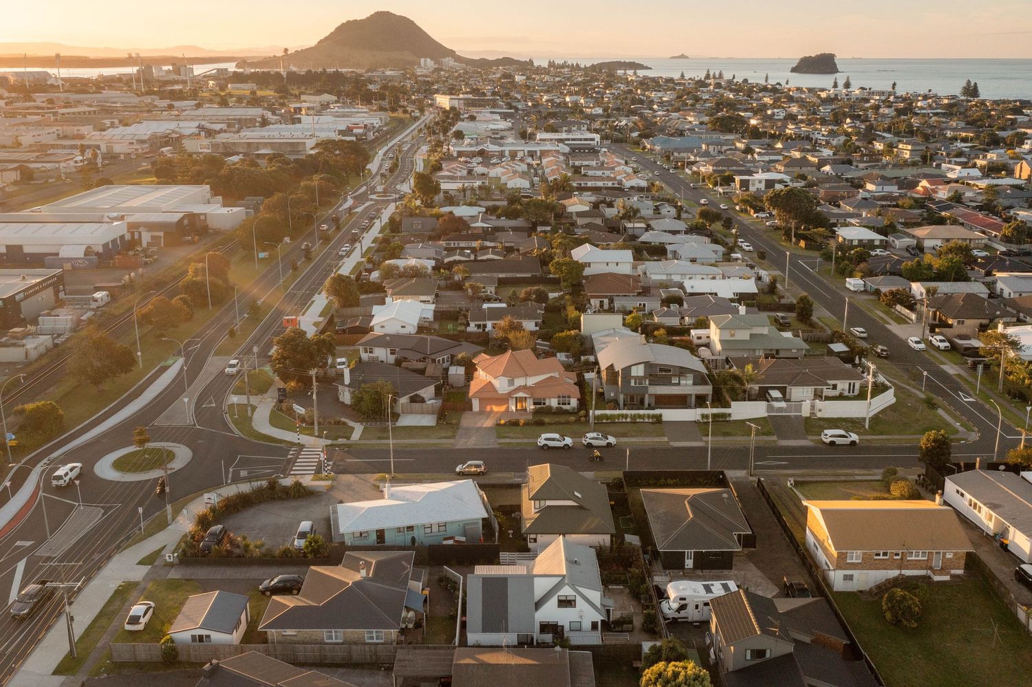 Panoramic aerial view of coastal town at sunset with residential houses and streets stretching along the shoreline.
