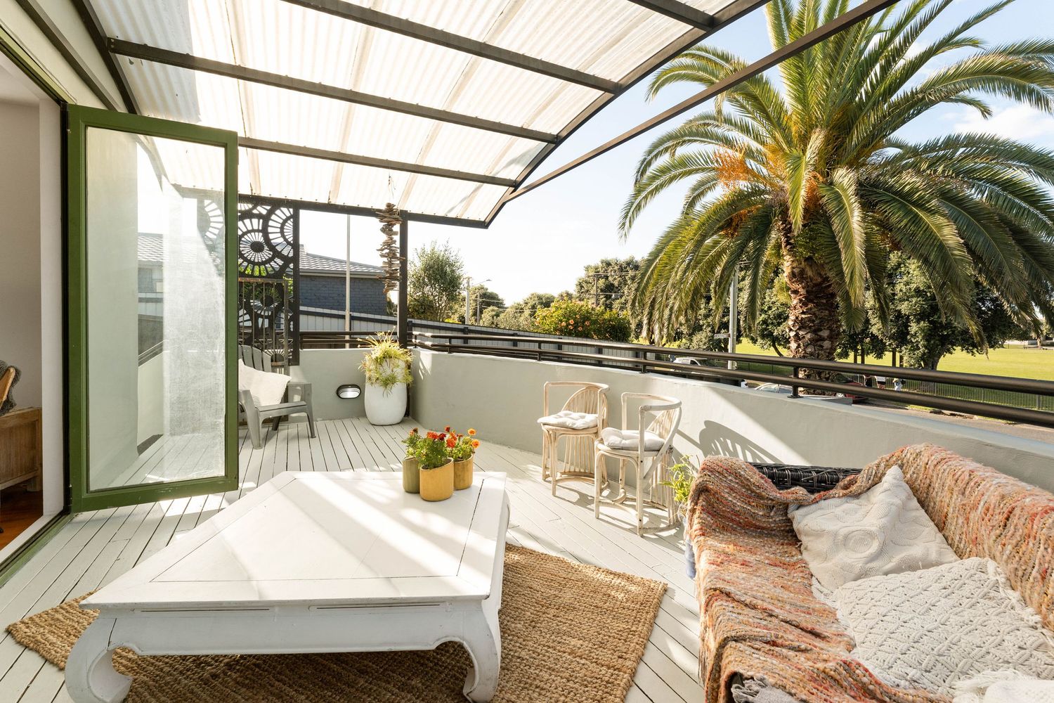 Covered outdoor patio area with white furniture surrounded by lush palm trees and tropical landscaping.
