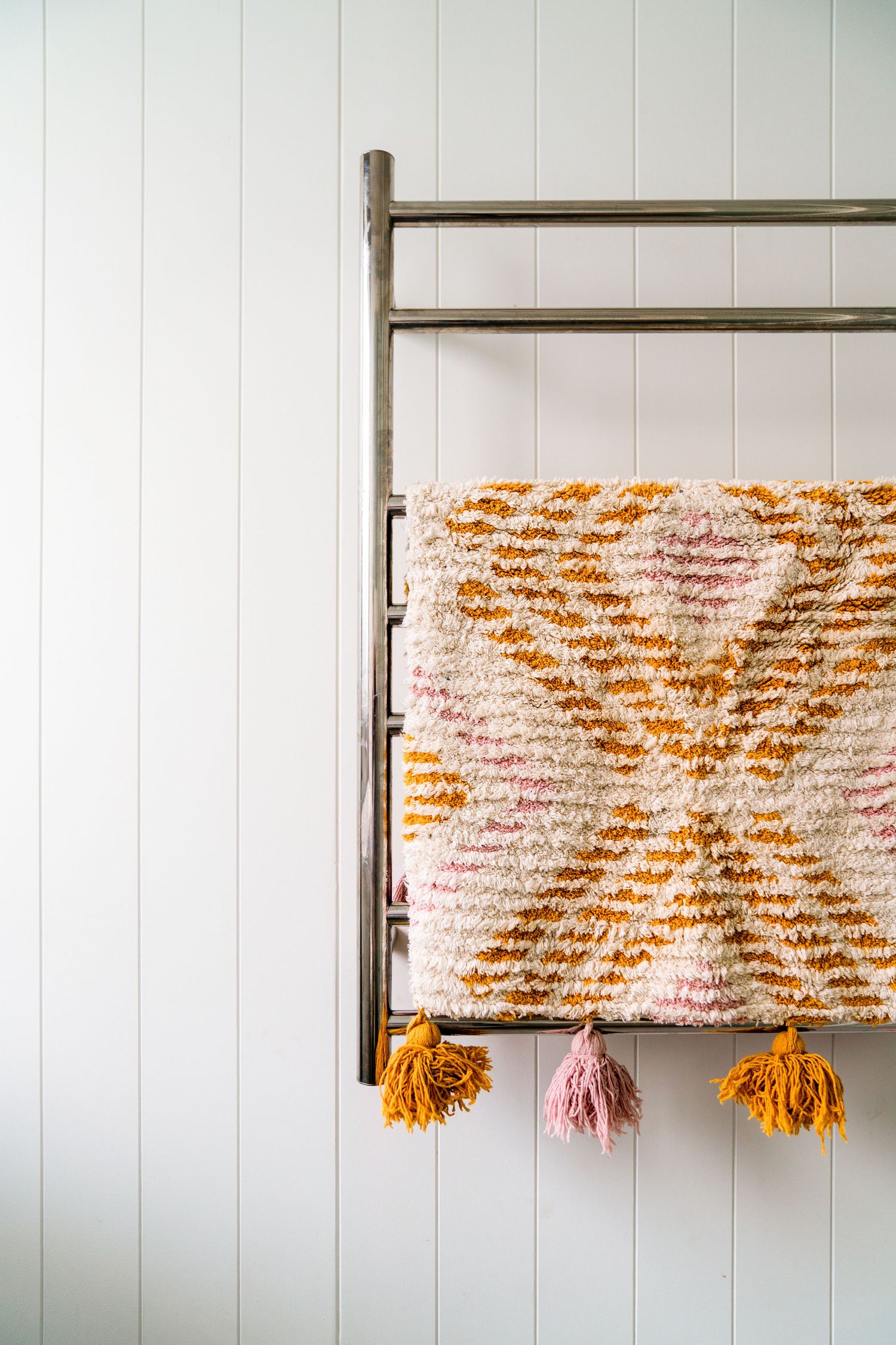 Textured throw blanket with orange and pink geometric pattern hanging on a metal rack.