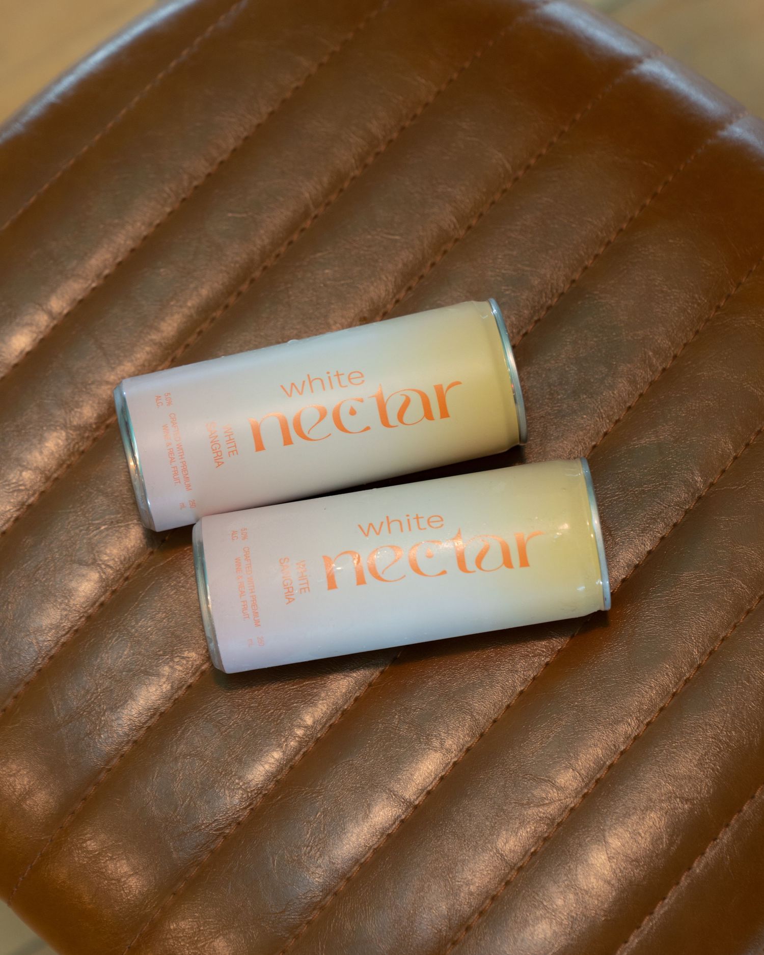 Two white lip balm or beauty product tubes with peach-colored text laying on a brown surface.