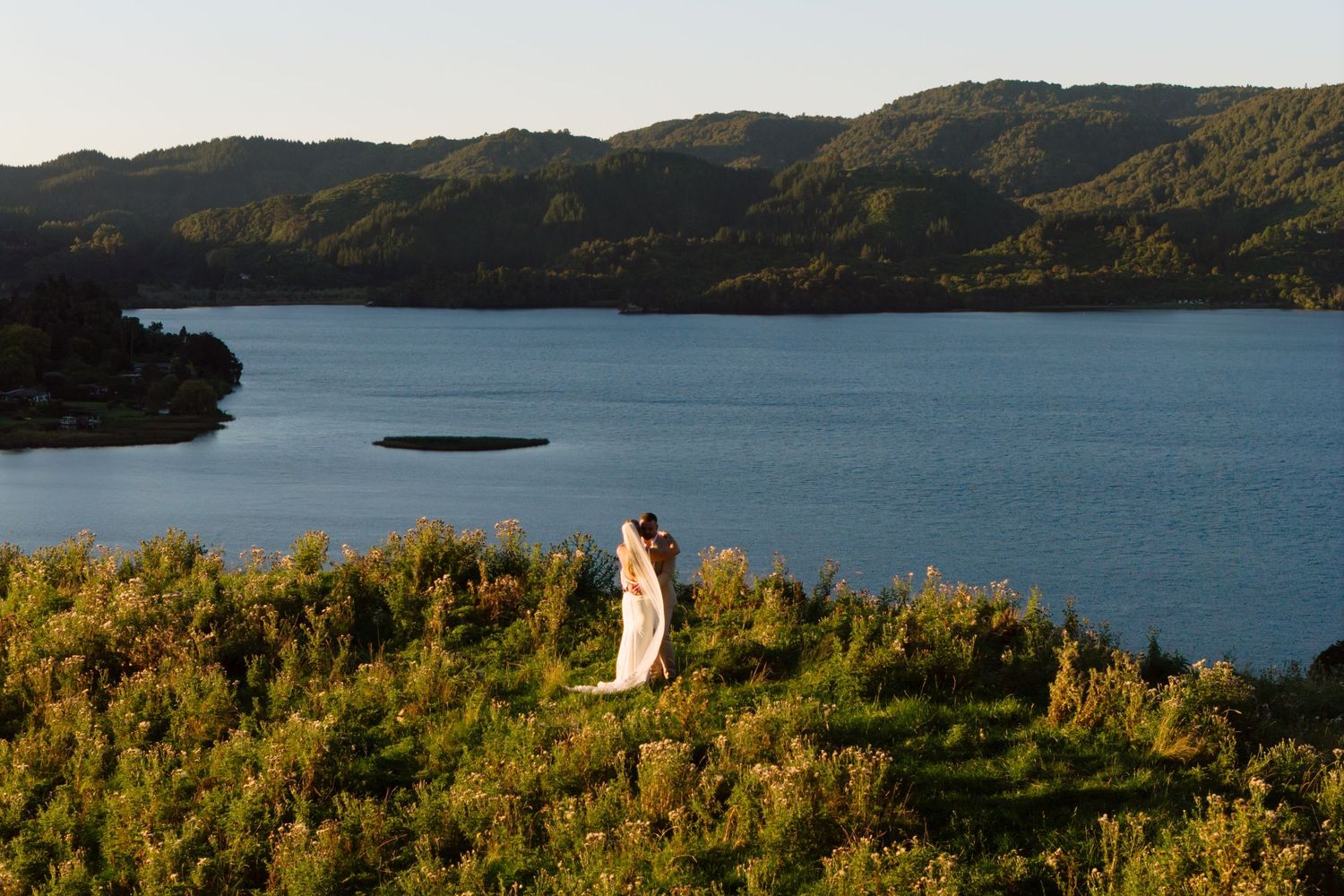 Panoramic view of a tranquil lake surrounded by rolling hills and lush vegetation in golden afternoon light.