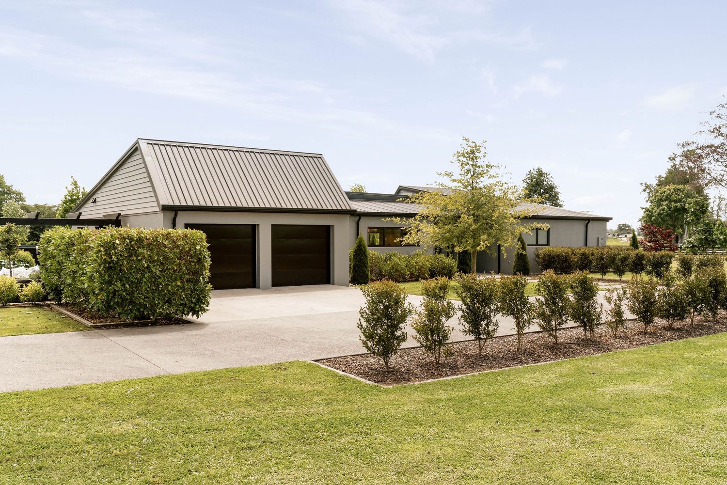 Modern ranch home exterior with attached two-car garage and landscaped garden featuring manicured hedges and lawn.