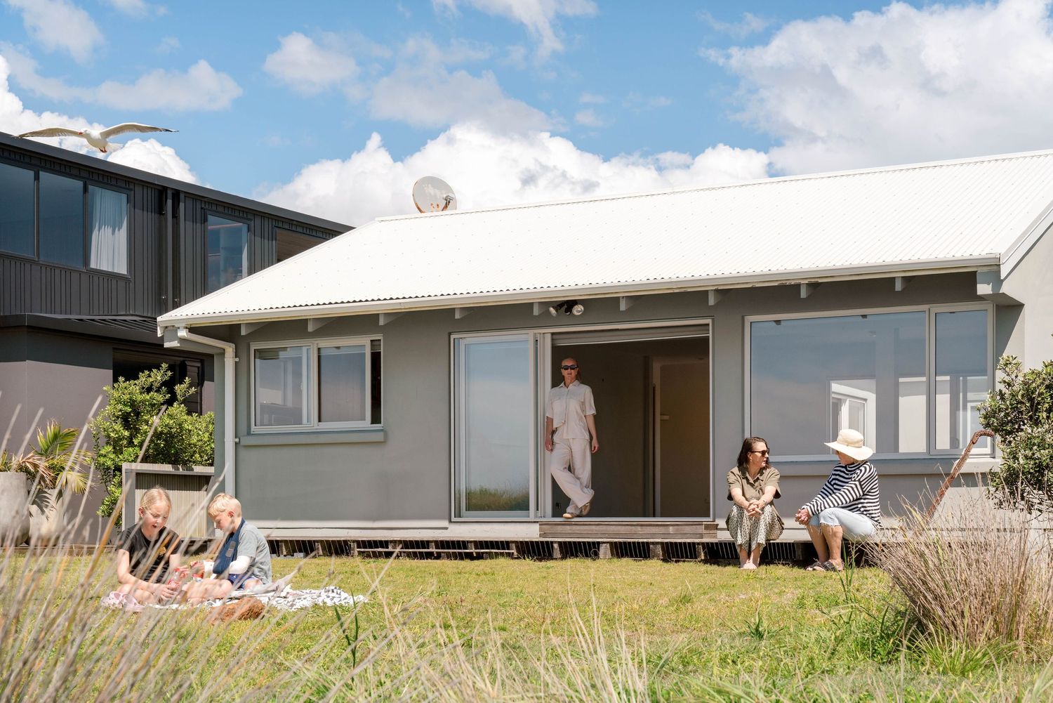 A small white beach house with a deck where people relax on a sunny summer day.