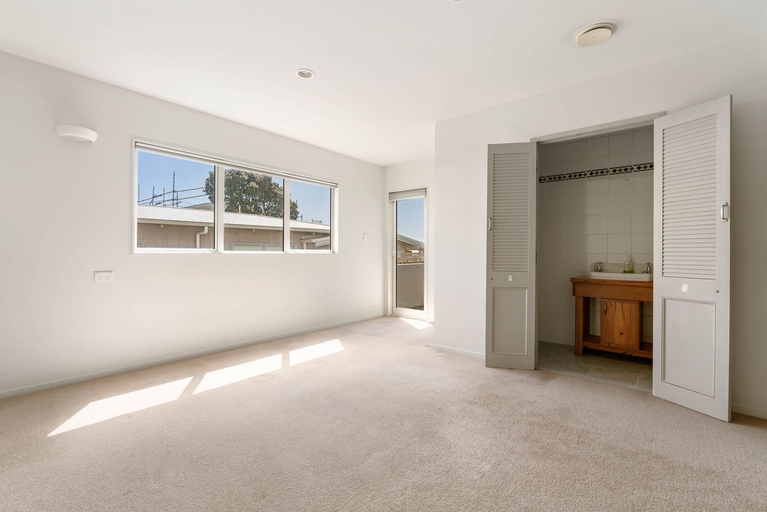 Bright bedroom with carpet flooring, white walls, and an adjoining bathroom visible.