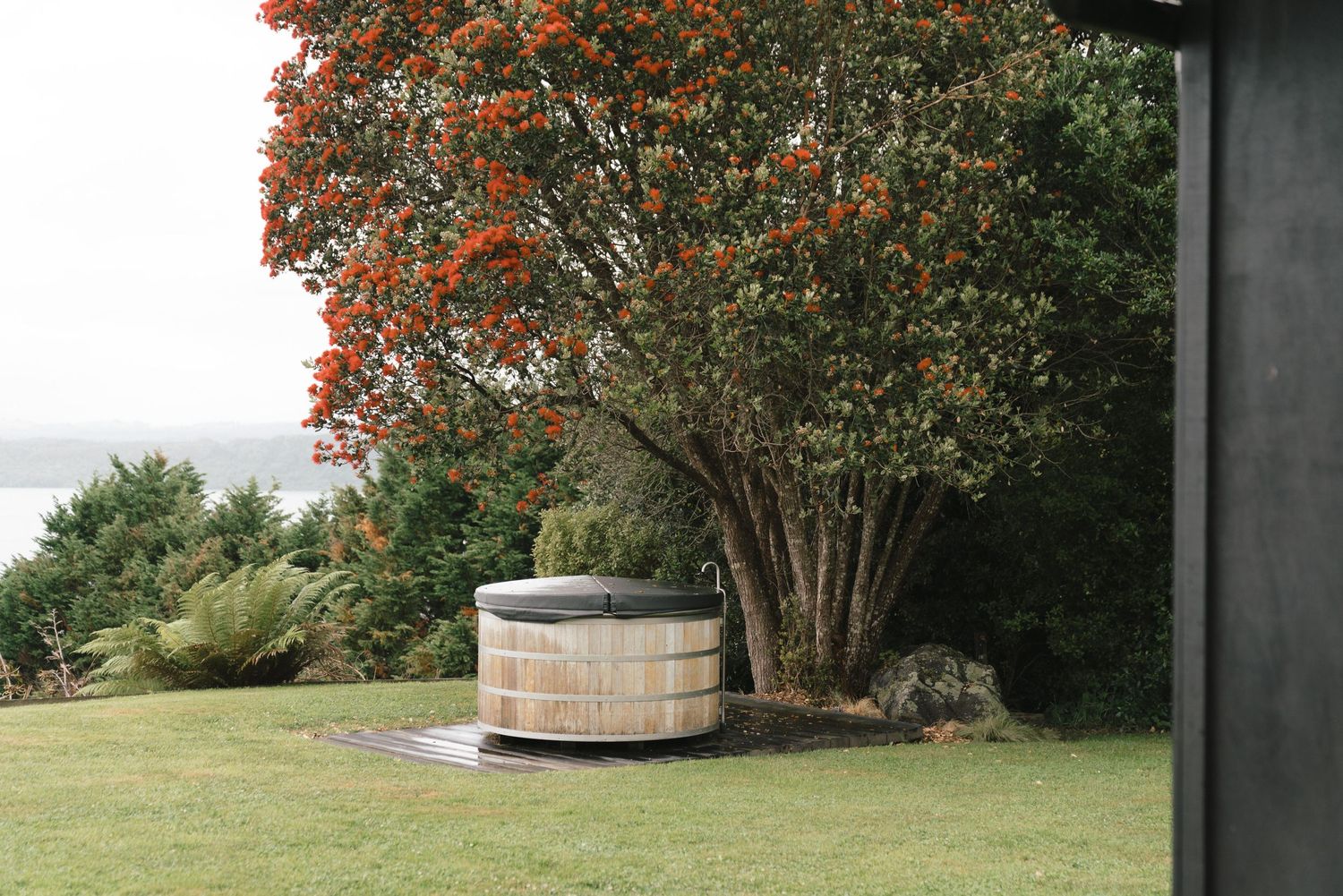 Fall trees with orange leaves surround a rustic wooden hot tub on the deck overlooking a serene ocean vista.