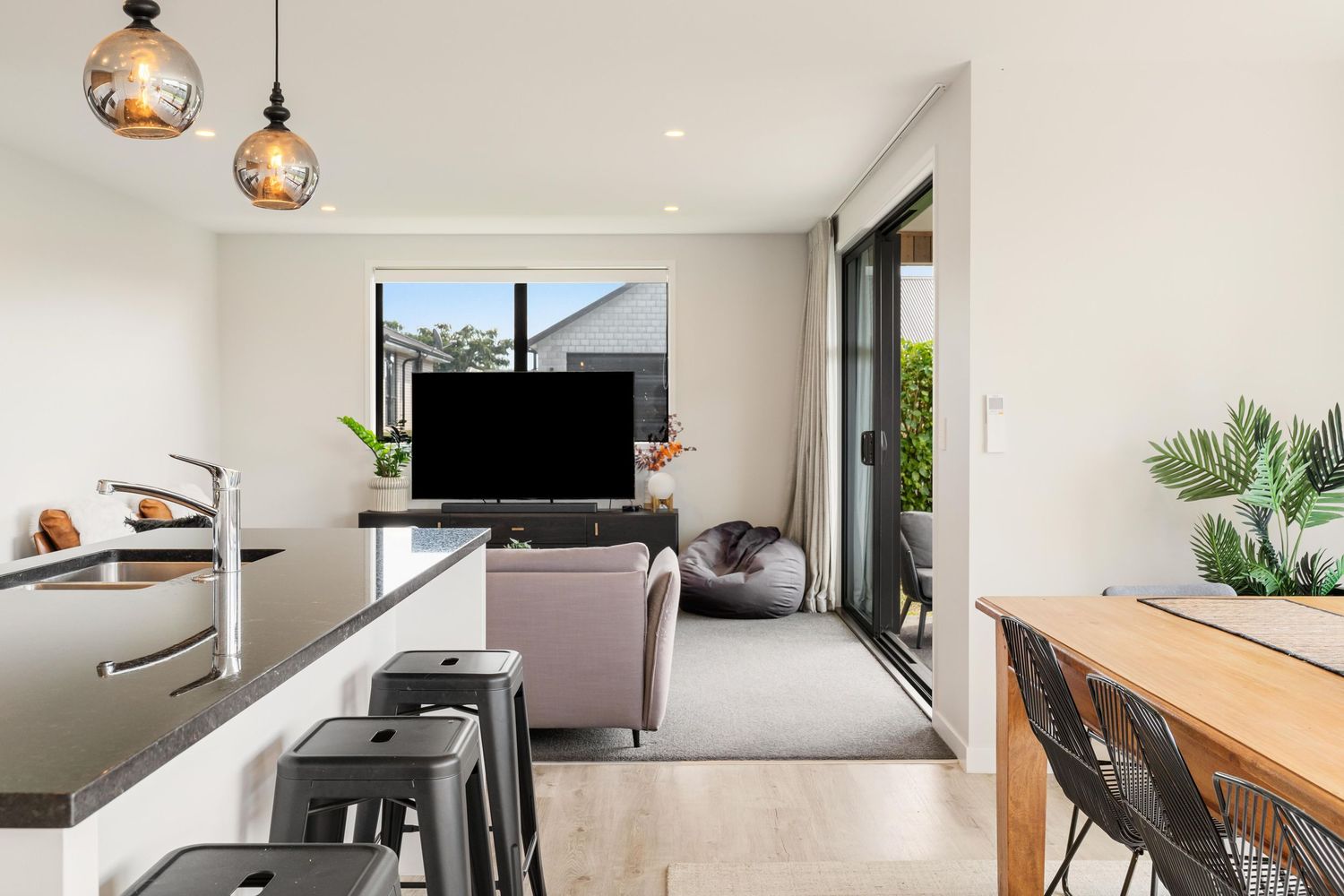 Contemporary open living space with hanging pendant lights, modern furniture and large TV mounted on white wall.