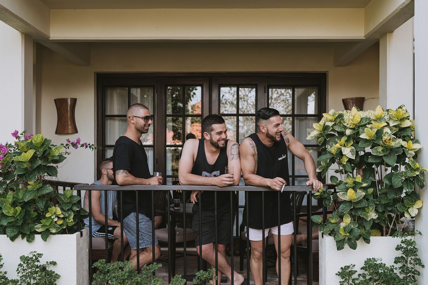 People relaxing on a covered patio with plants and outdoor furniture.