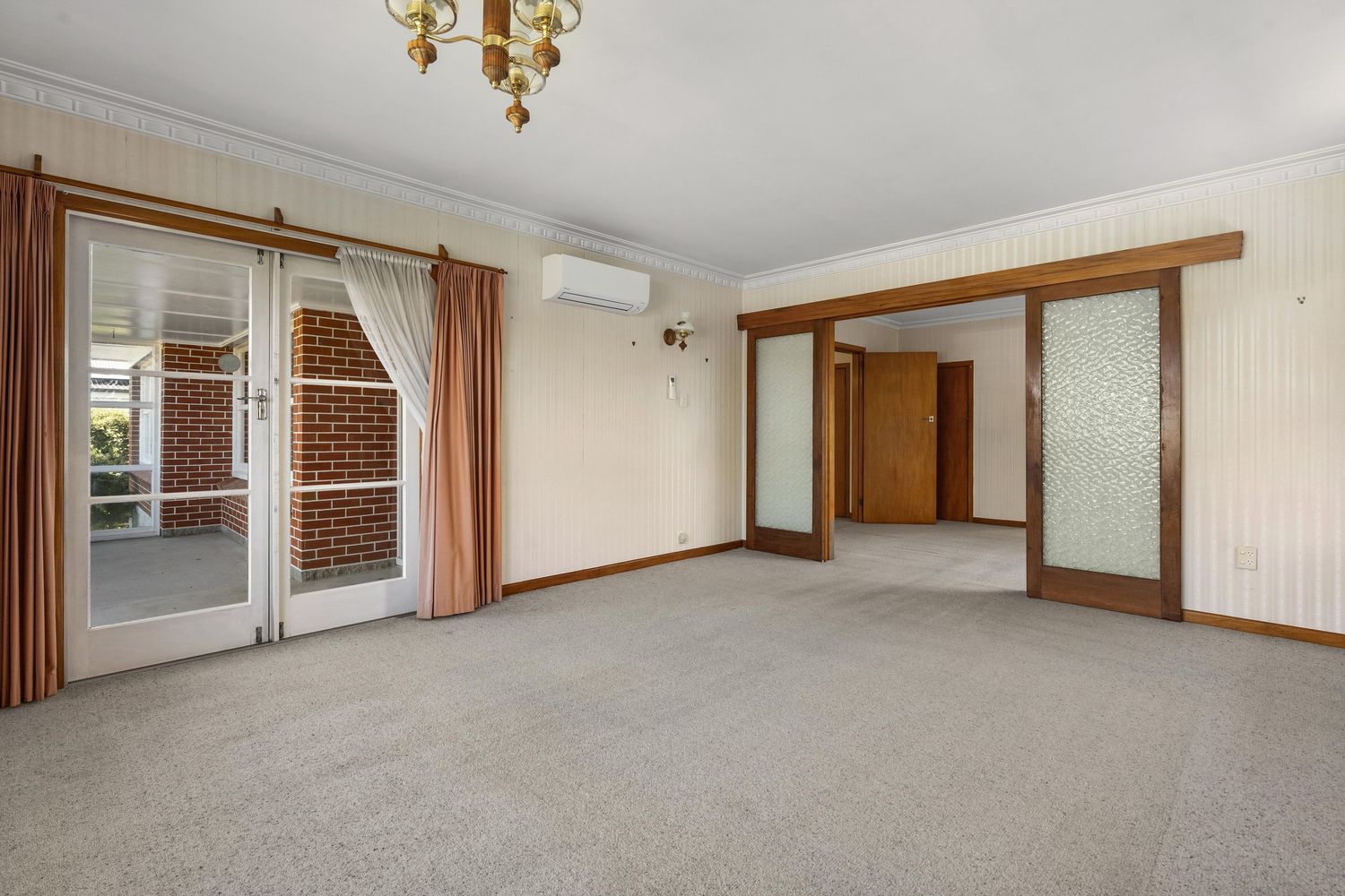 Spacious carpeted living room with beige walls and classic brass chandelier.
