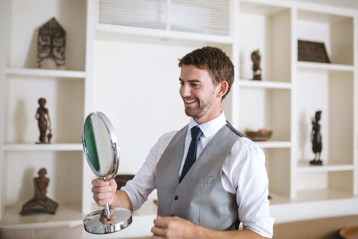 A businessman in a gray vest works at his desk in a bright modern office with white built-in shelving.