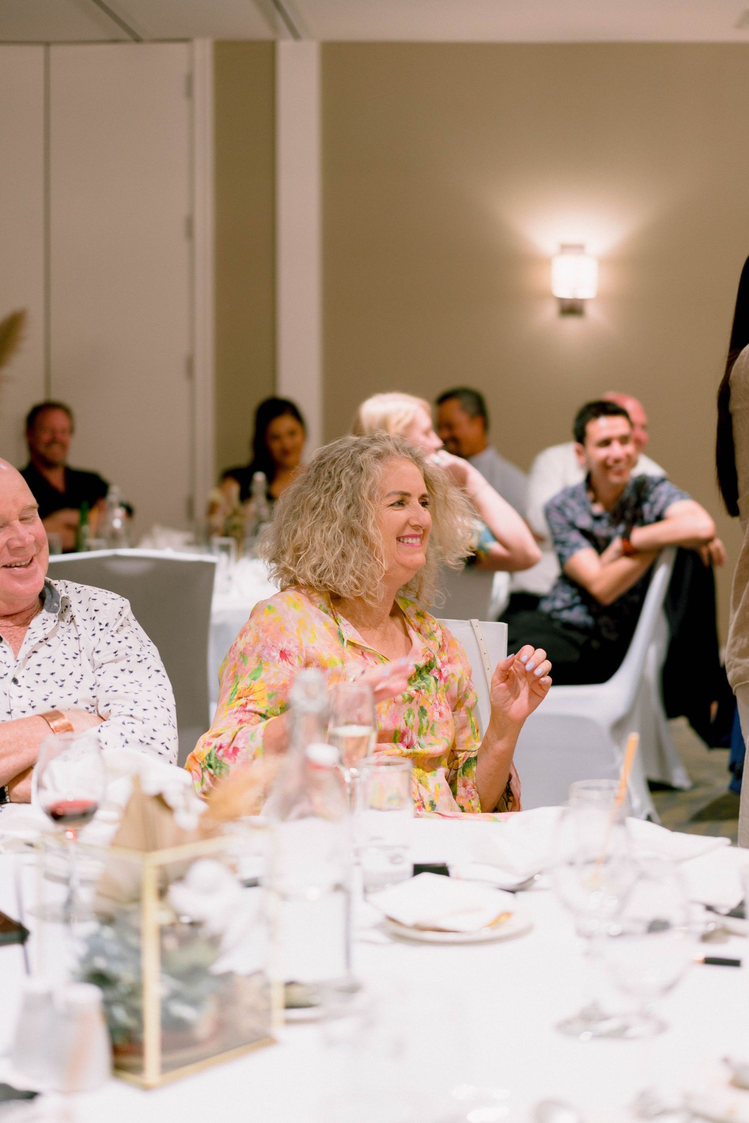 Wedding reception guests enjoying dinner and conversation at elegant white-clothed tables.