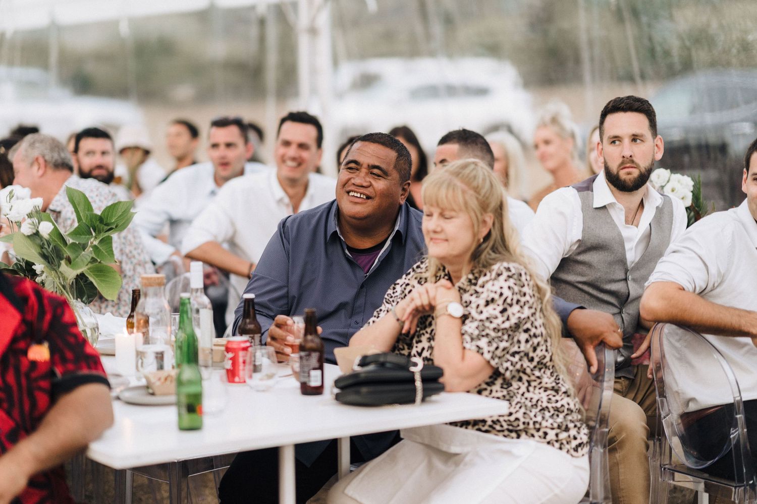 Wedding reception guests enjoying refreshments at tables under tent covering.