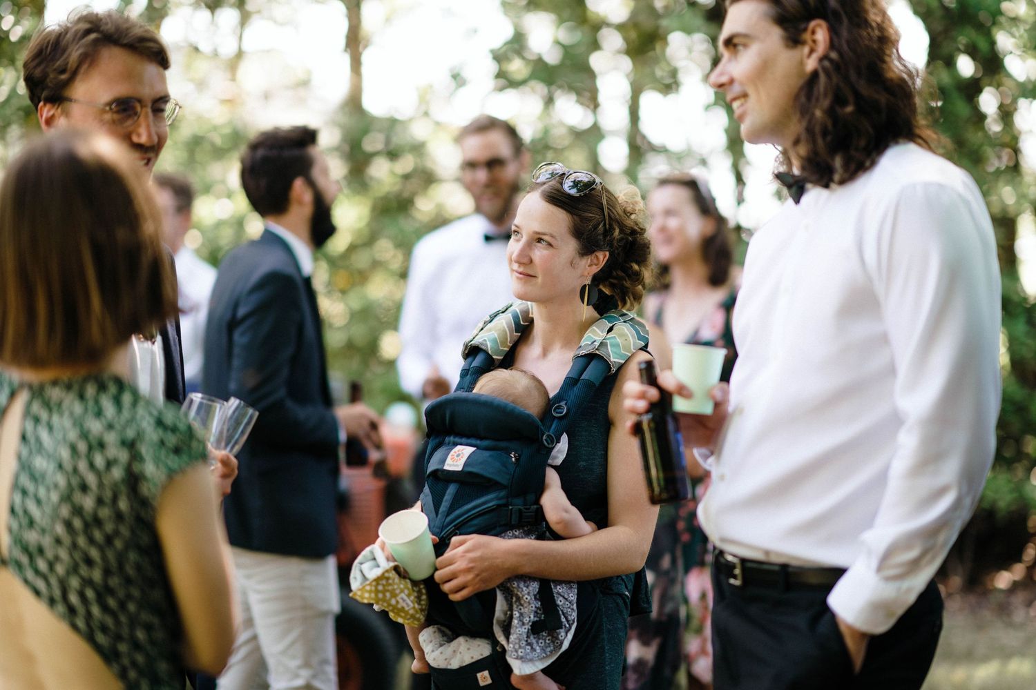 Outdoor wedding reception with guests socializing under natural greenery.