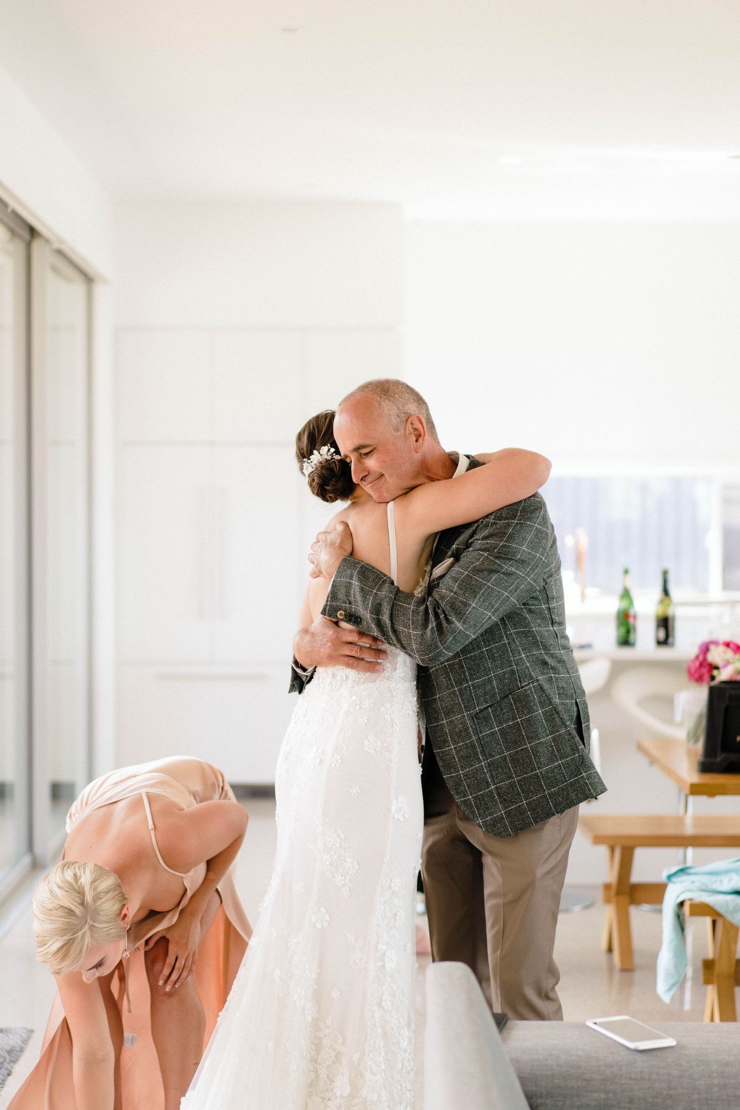 Emotional wedding gathering in a bright white room with natural lighting streaming through windows.