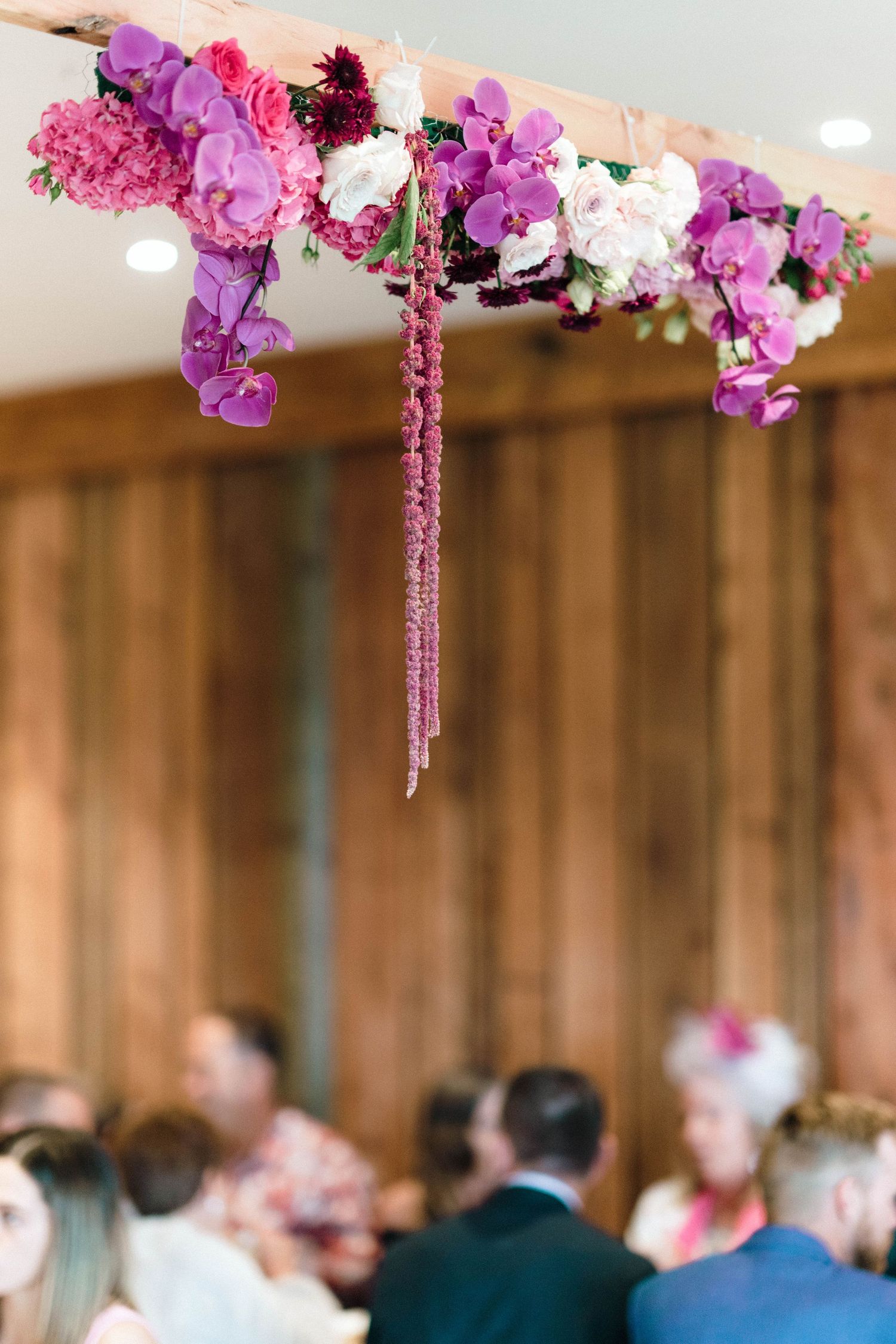 Purple and pink floral arrangements hanging from the ceiling at an indoor wedding reception.