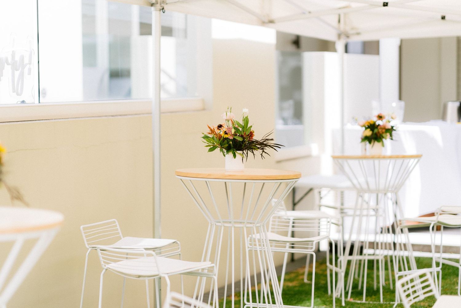 Modern cafe interior with white metal chairs and round wooden tables decorated with floral centerpieces.
