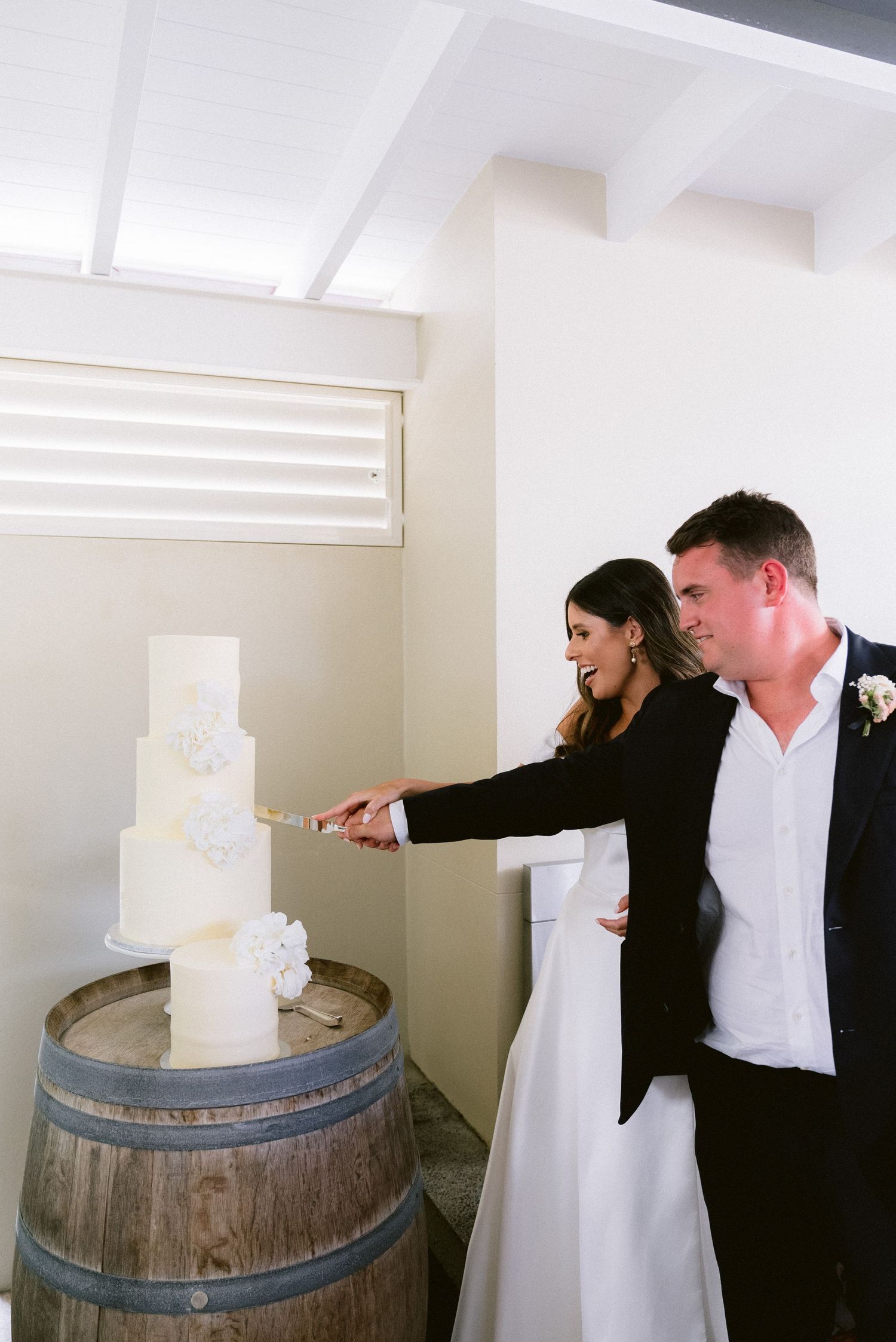 Wedding cake cutting sequence on rustic wine barrel display in bright indoor setting.