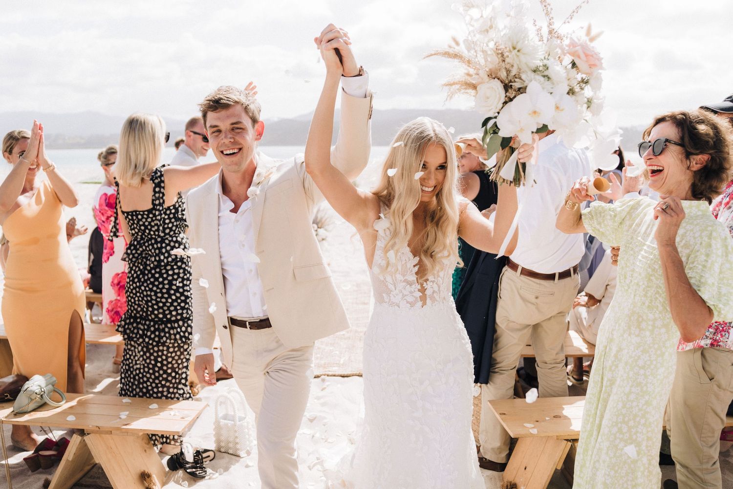 Joyful celebration on a sunny beach with elegant wedding attire and decorations.