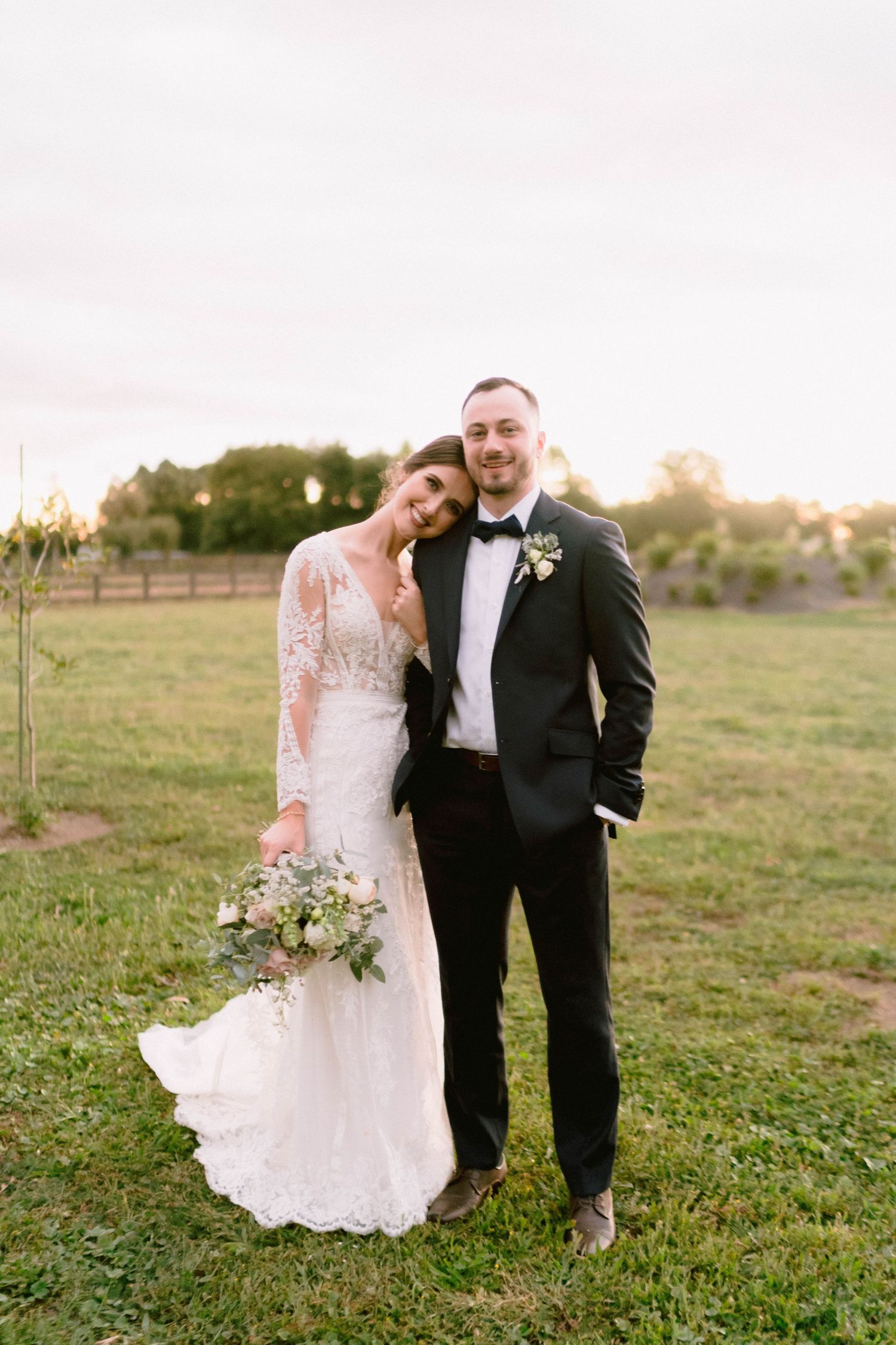 A romantic outdoor wedding portrait of a newlywed couple at sunset in a countryside setting.
