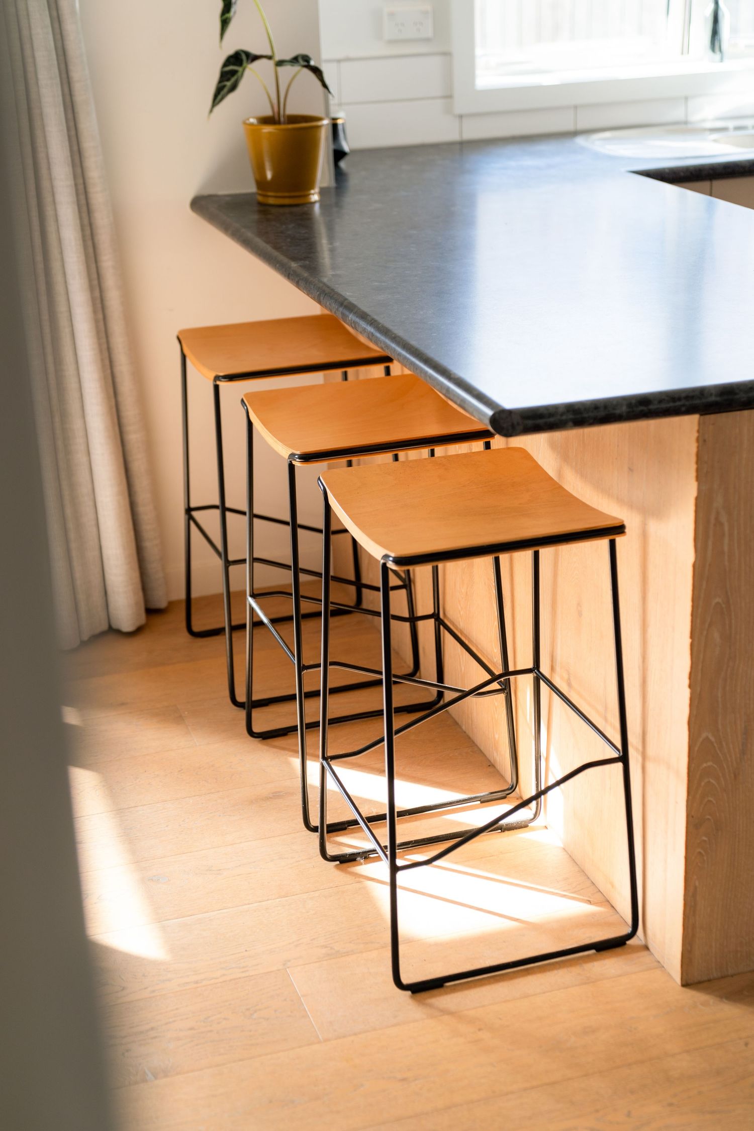 Series of minimalist nesting tables with wooden tops and black metal frames in a sunlit room.